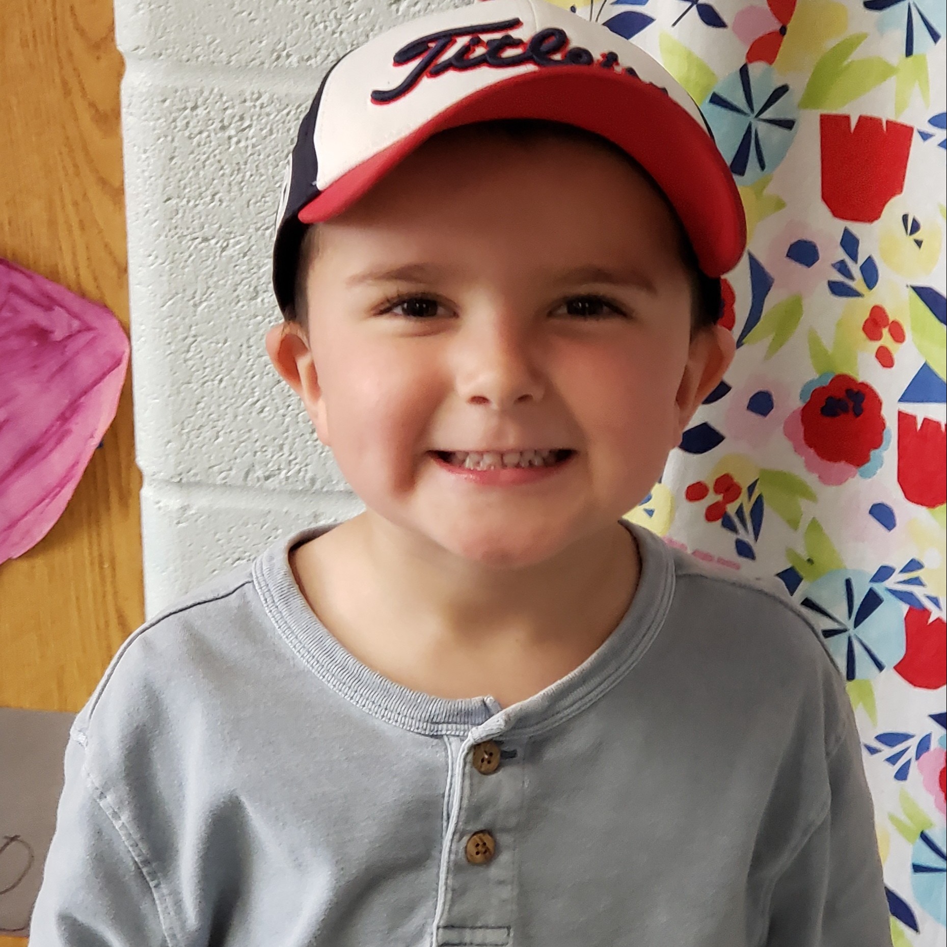 smiling little boy with a red-white-&-black cap wearing a gray henley