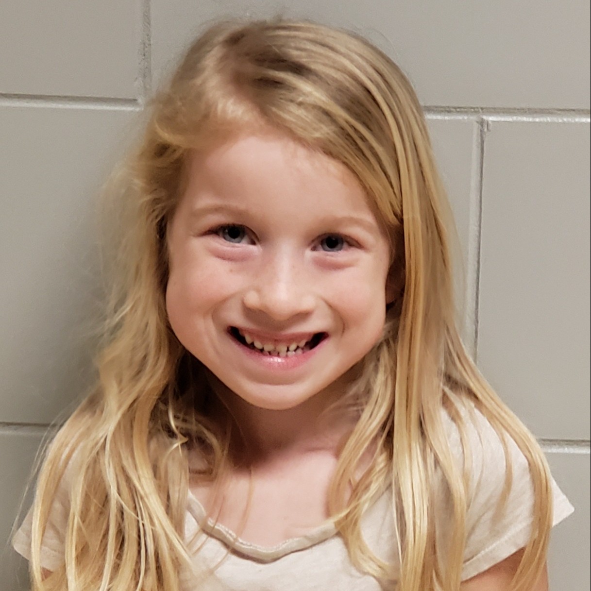 smiling young girl with blonde hair wearing a white t-shirt