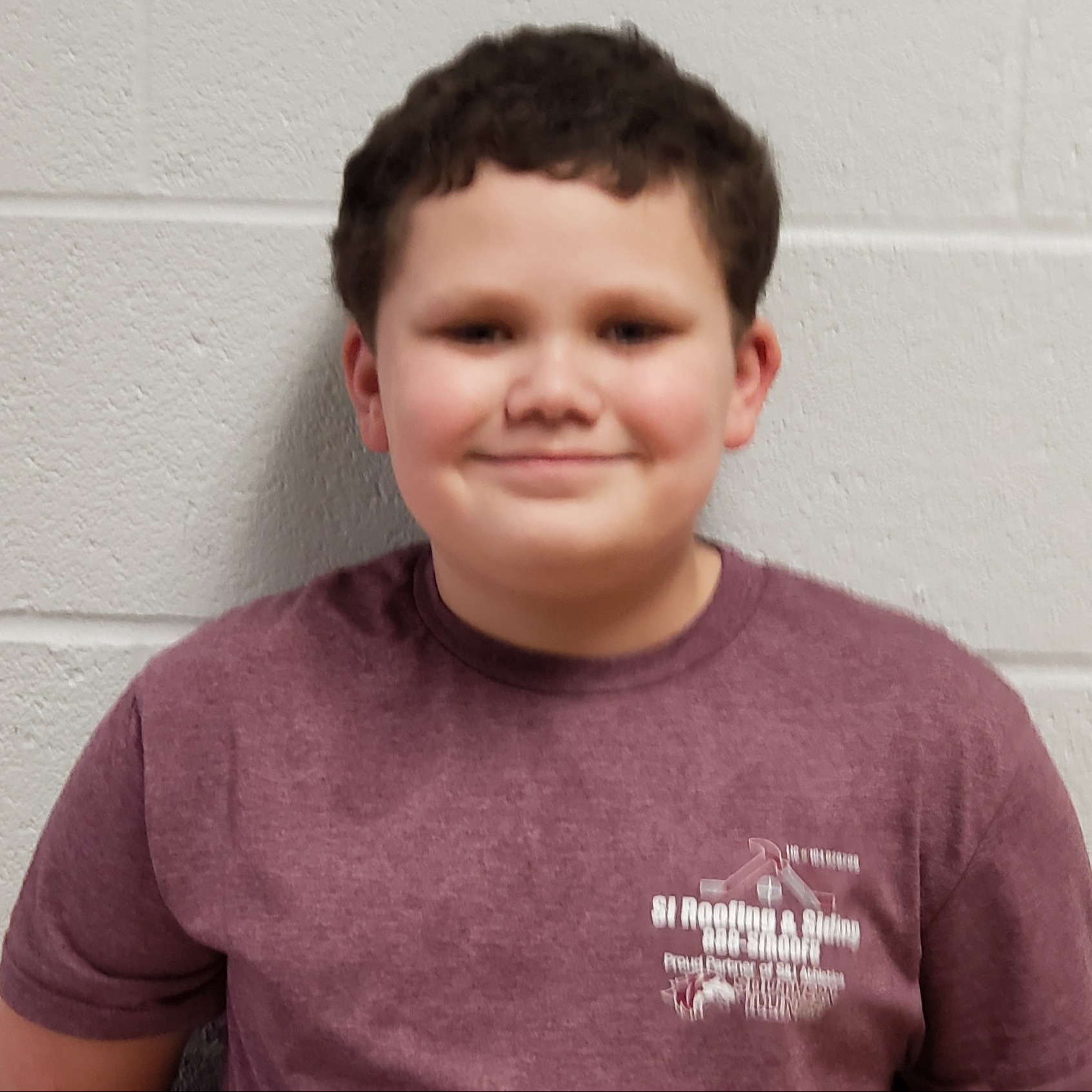 smiling boy with dark curly hair wearing a maroon t-shirt