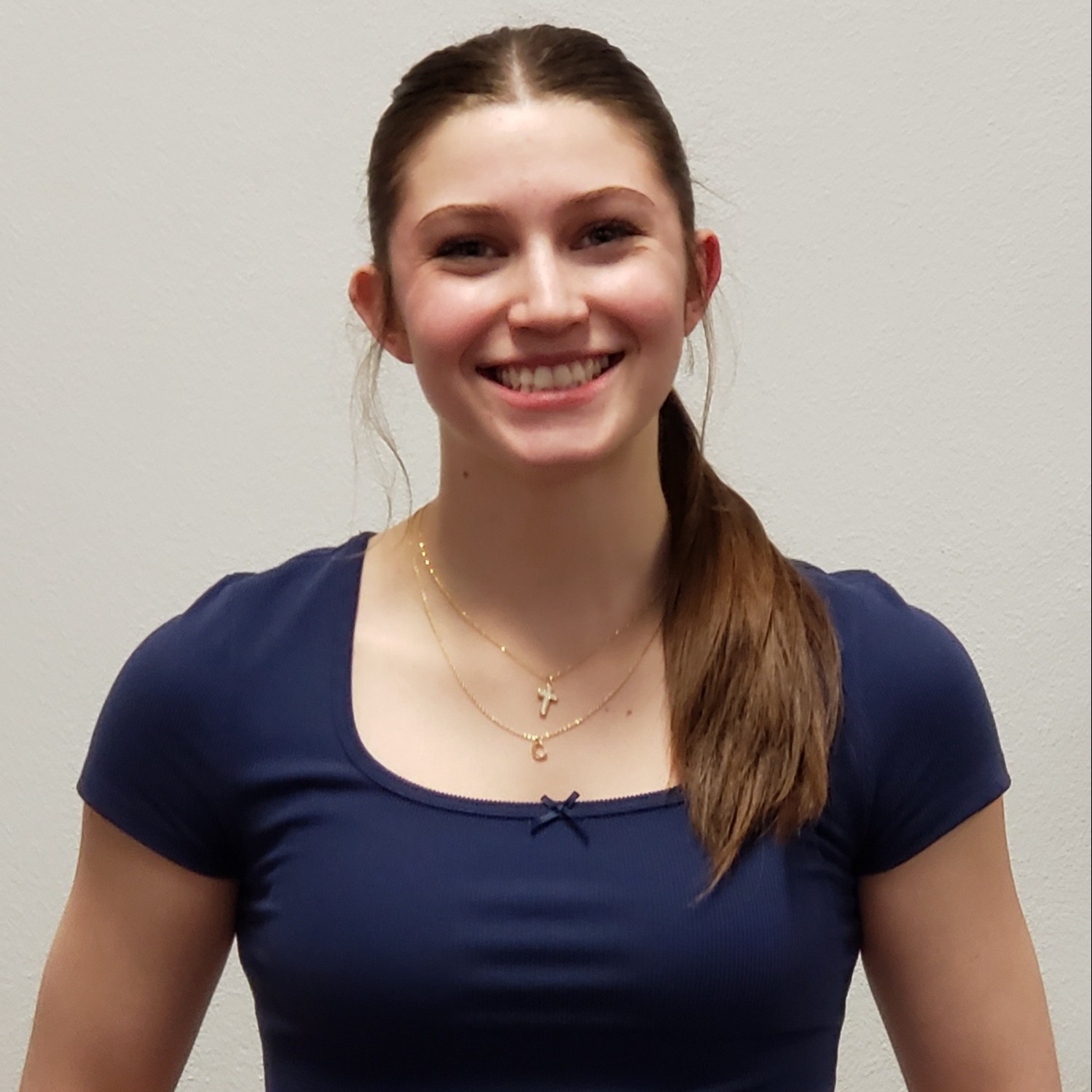 smiling young lady with dark hair pulled back wearing a cross necklace and blue t-shirt