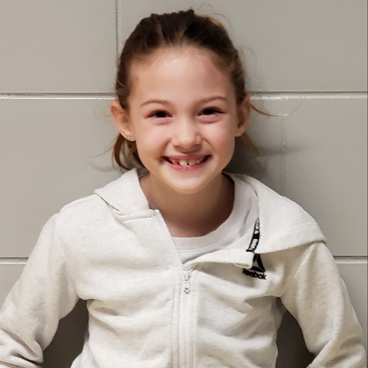 smiling girl with dark hair pulled back wearing a white zipped jacket over a white t-shirt