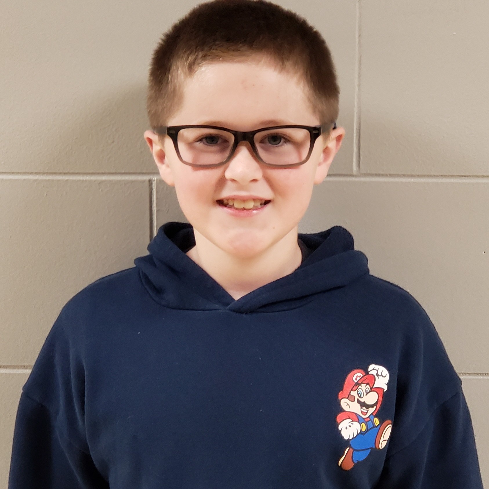 smiling boy with dark hair and glasses wearing a navy hoodie with Mario on it