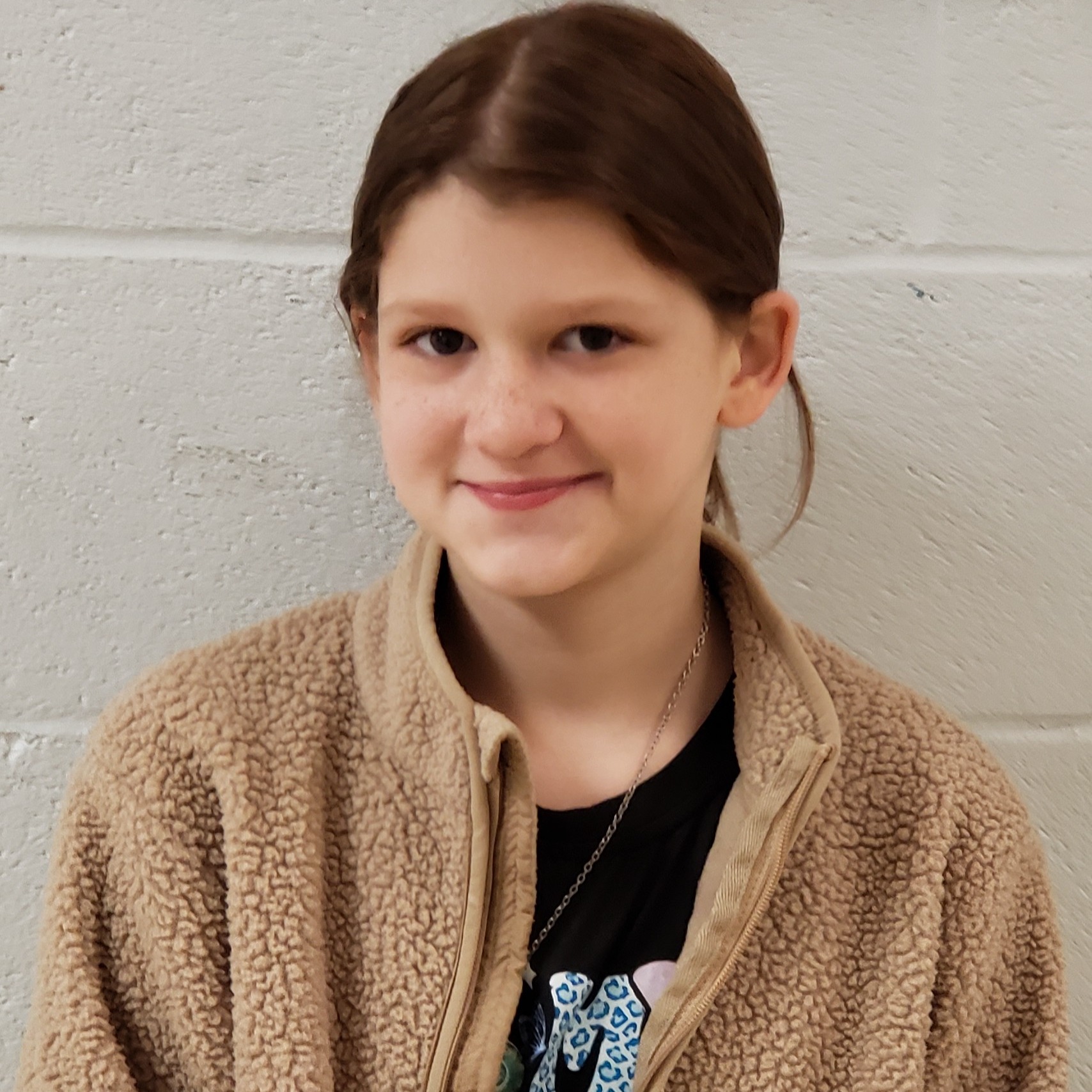 smiling girl with dark hair pulled back wearing a black t-shirt under a beige sherpa jacket