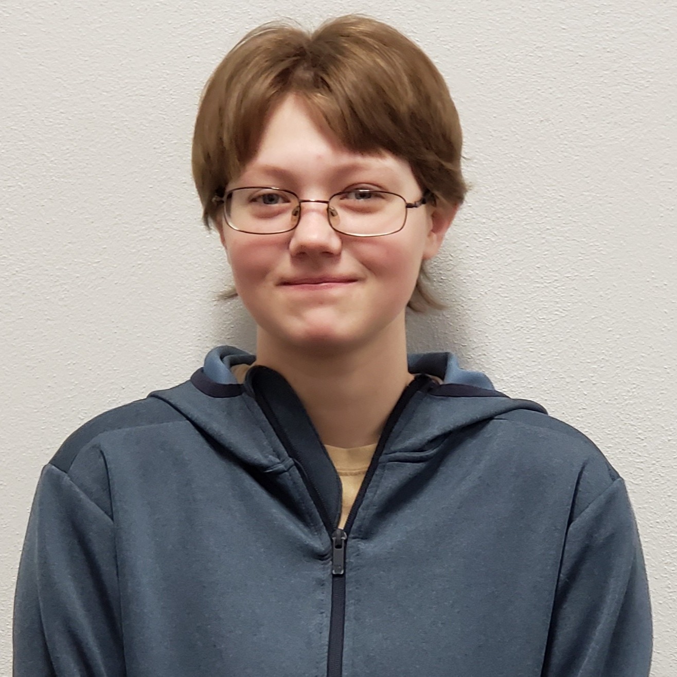 grinning young lady with dark blonde hair wearing a beige t-shirt under a blue jacket