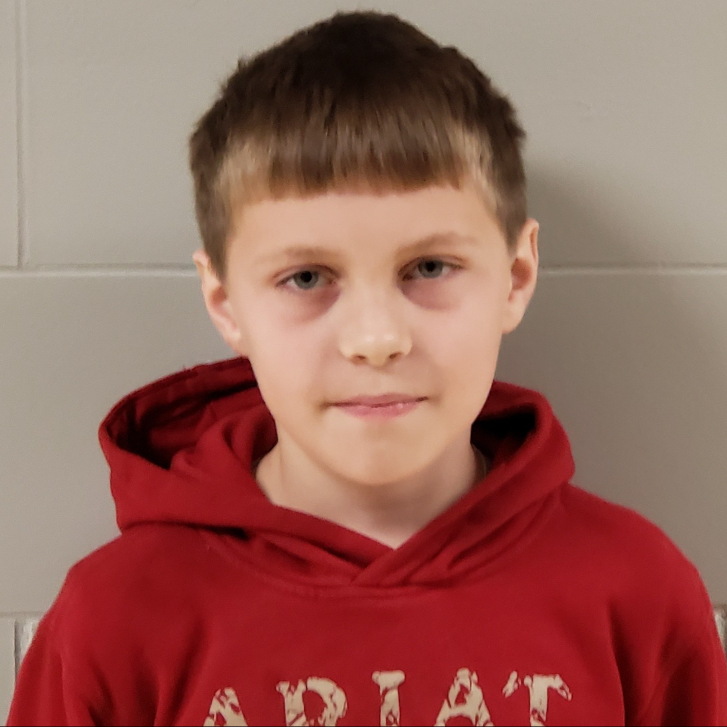 smirking boy with dark hair wearing a red hoodie