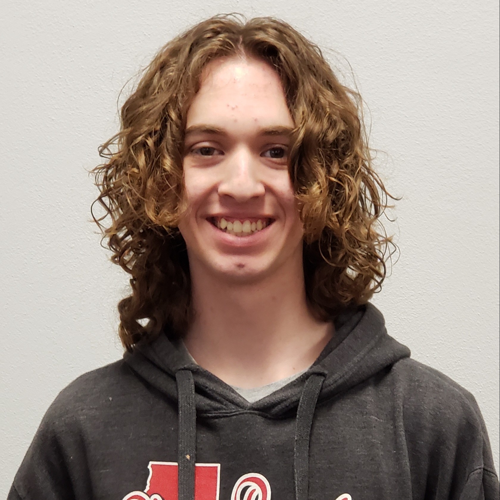 smiling young man with curly dark blonde hair wearing a dark gray hoodie