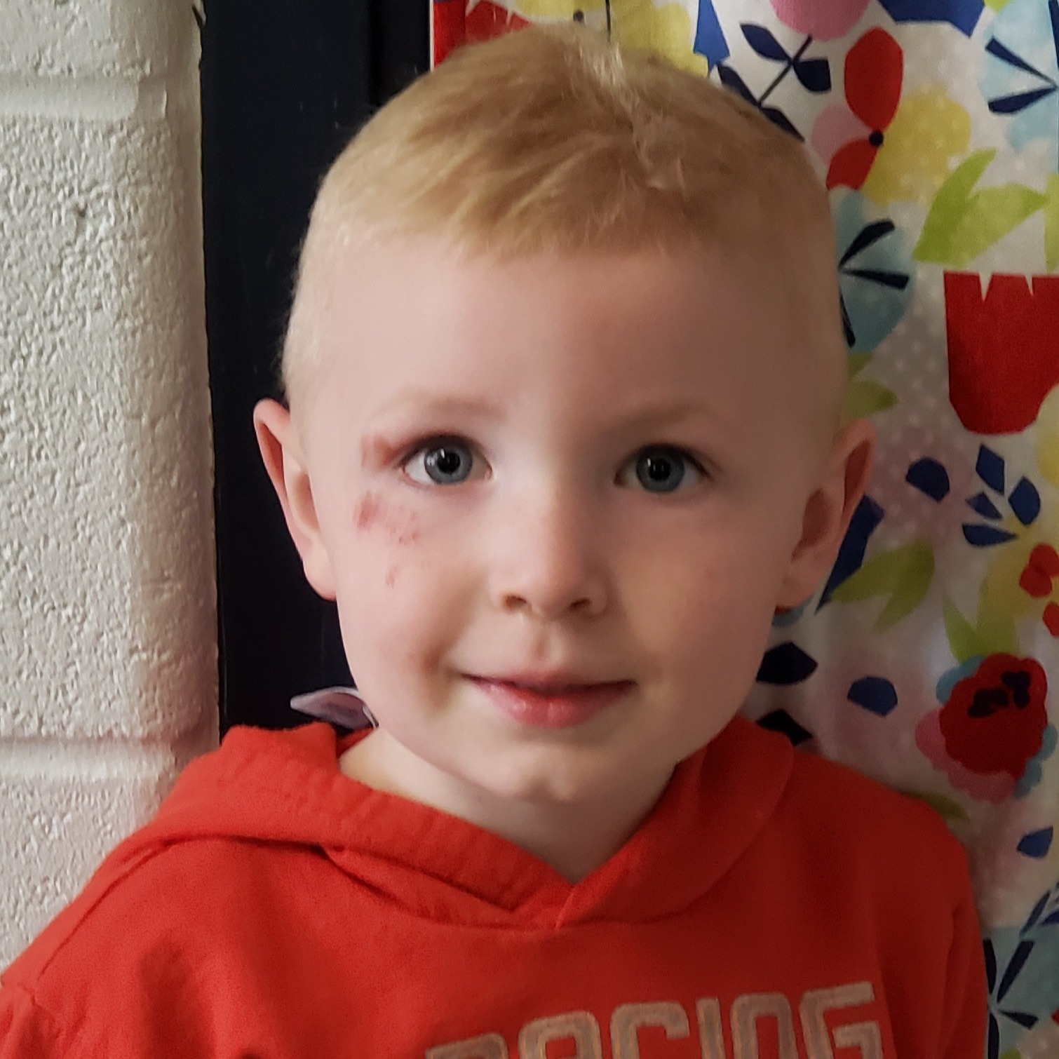 smiling little boy with blonde hair wearing a red hoodie