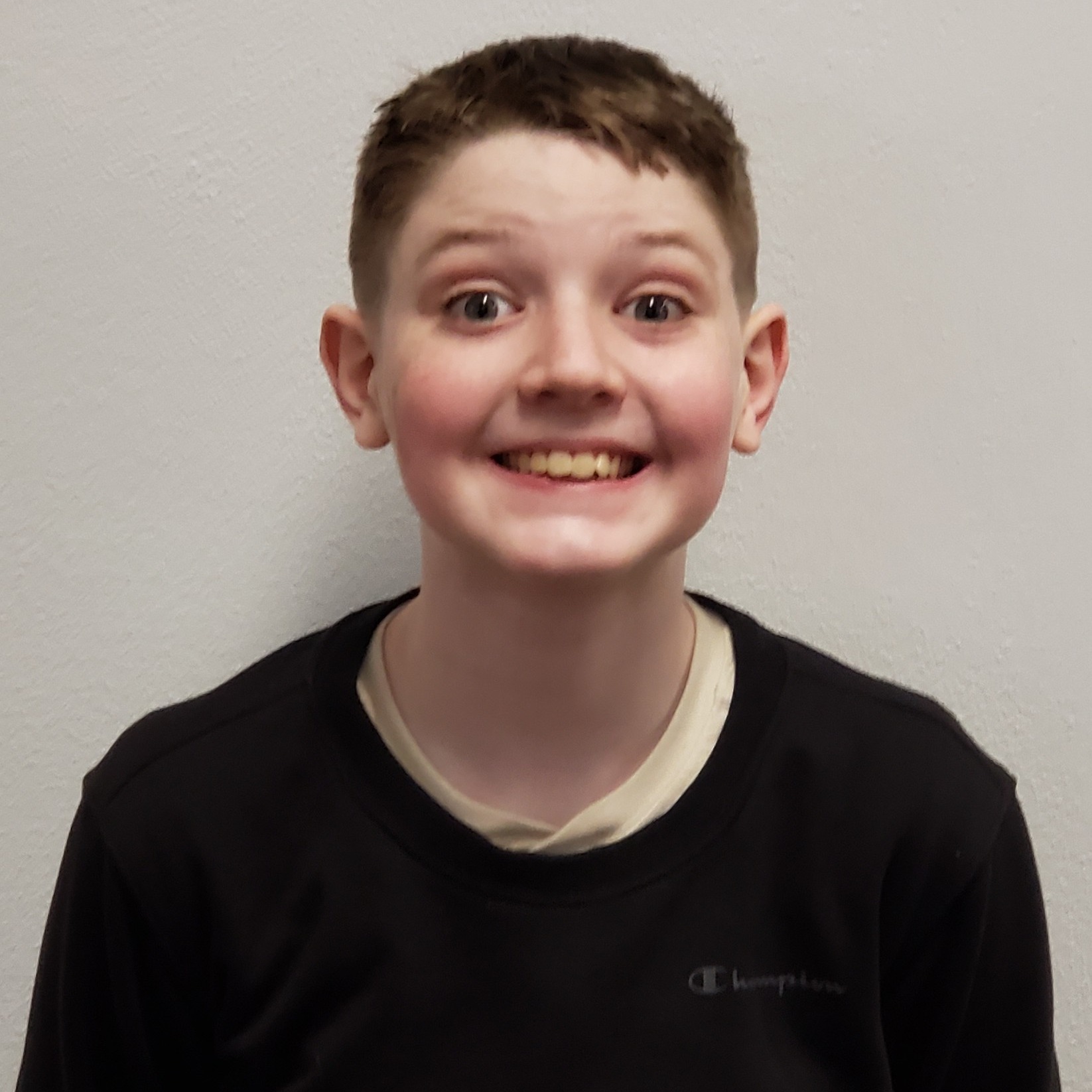 smiling boy with dark hair wearing a black sweatshirt over a cream t-shirt