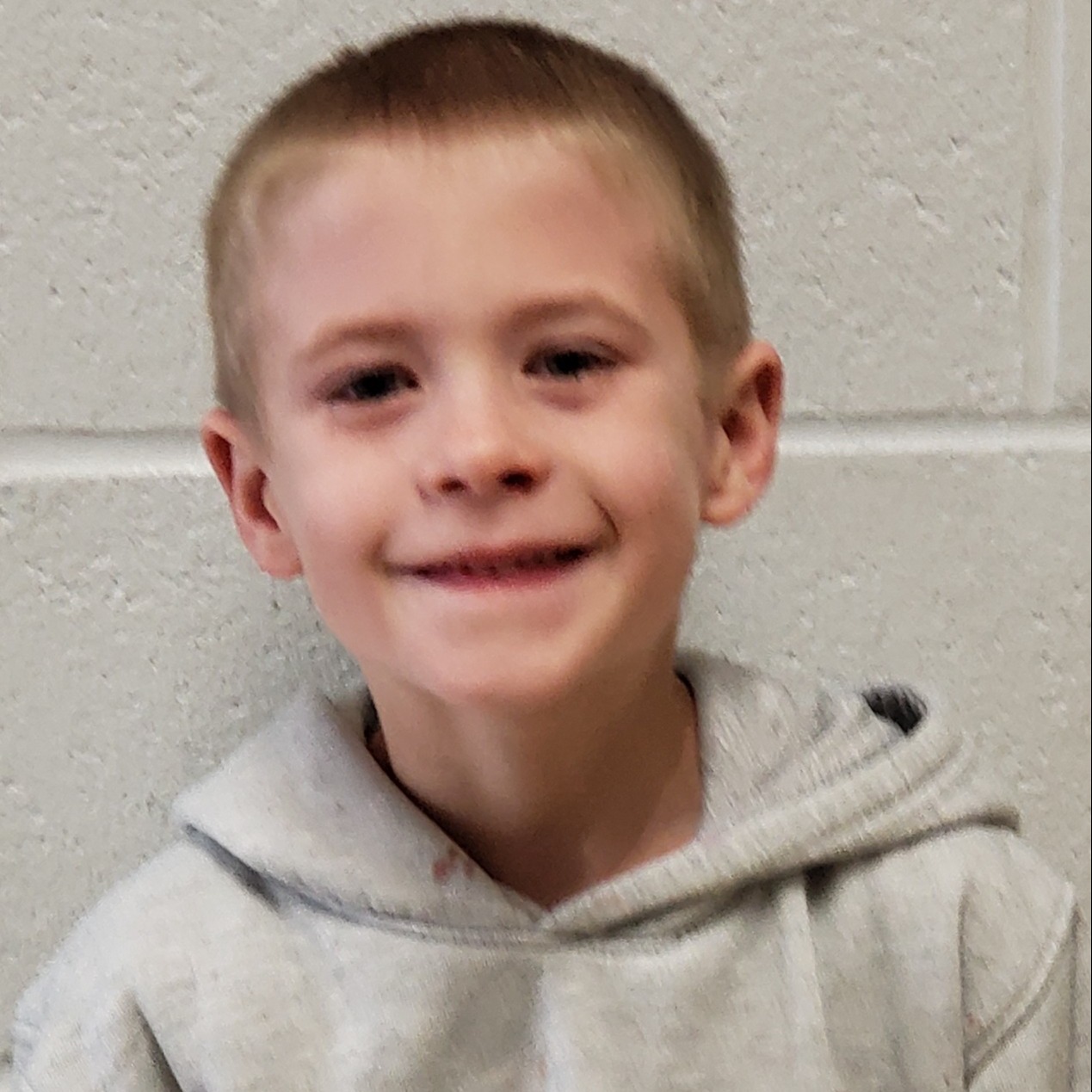 smiling boy with blonde hair wearing a gray hoodie