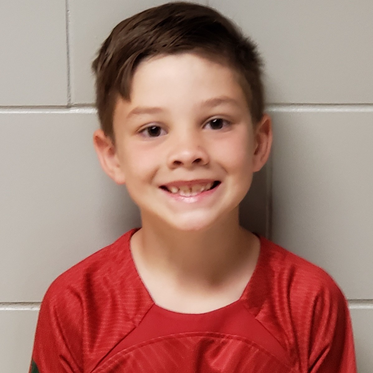 smiling boy with dark hair wearing a red soccer shirt