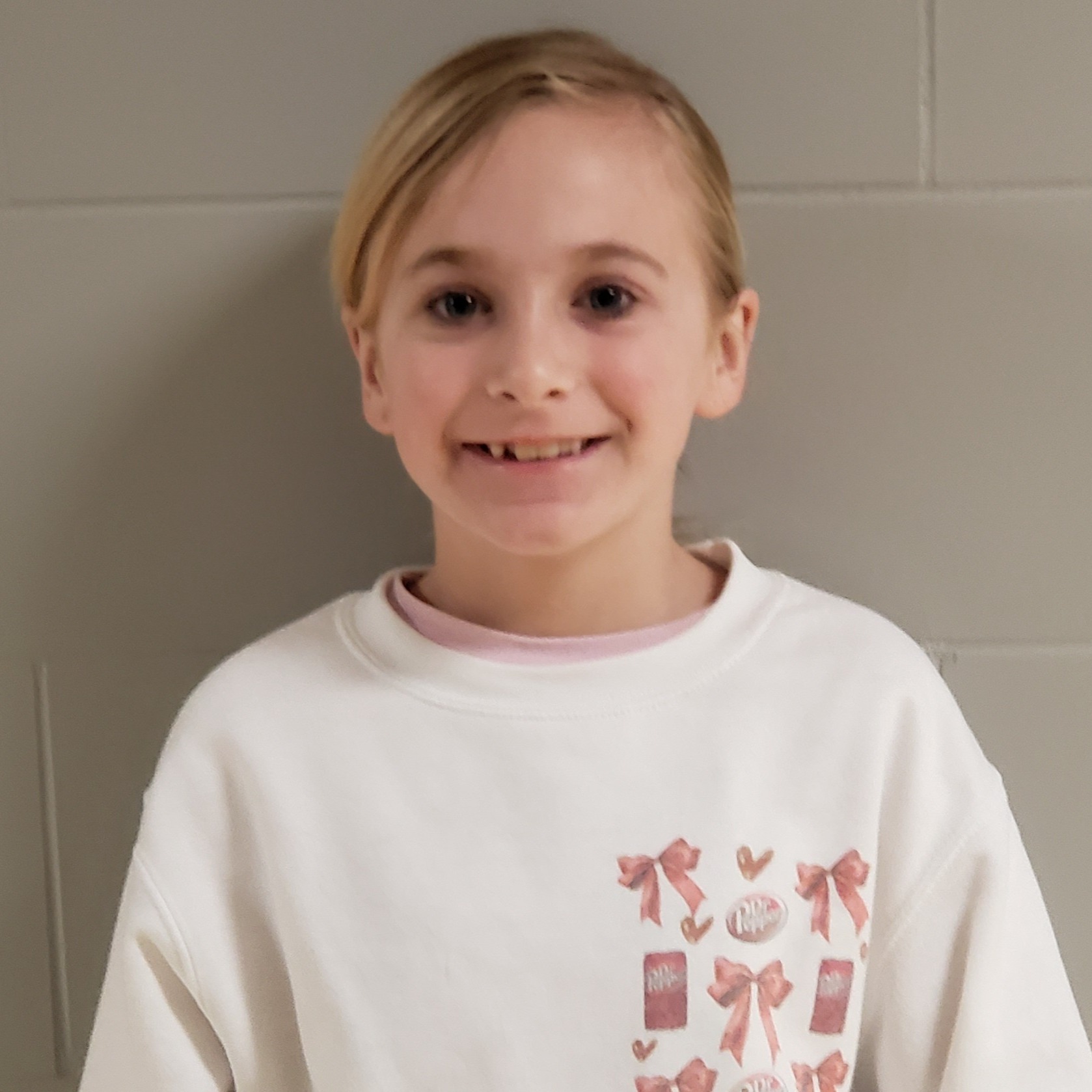 smiling girl with blonde hair pulled back wearing a white sweatshirt