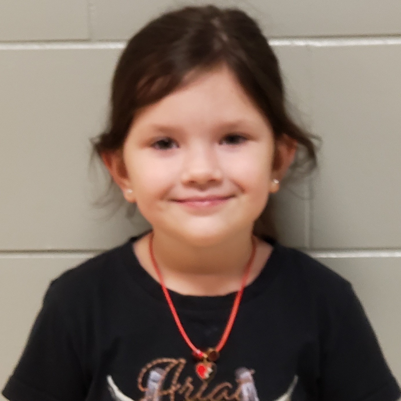 grinning young girl with dark hair pulled back wearing a black t-shirt and red necklace