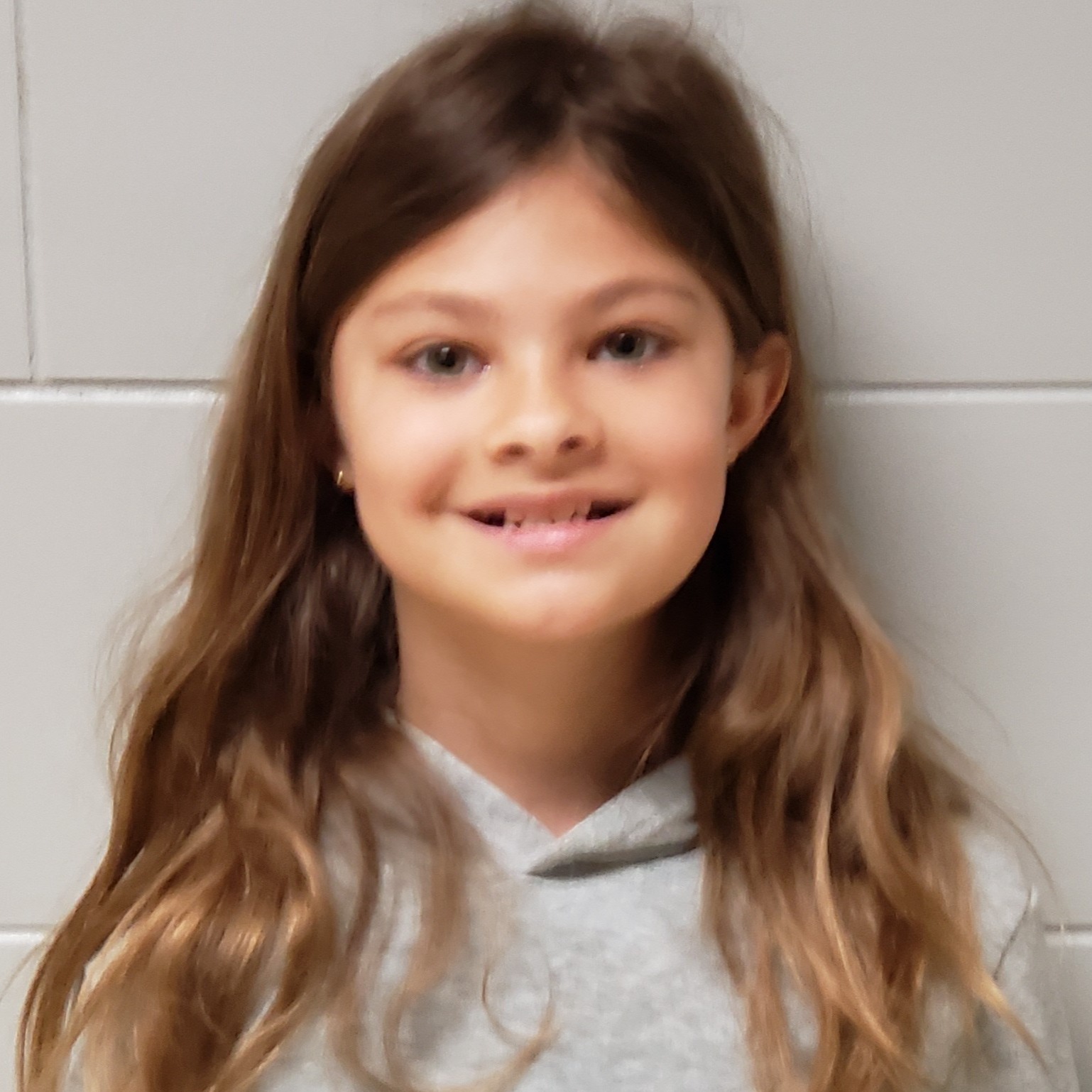 smiling girl with long brown hair wearing a gray hoodie