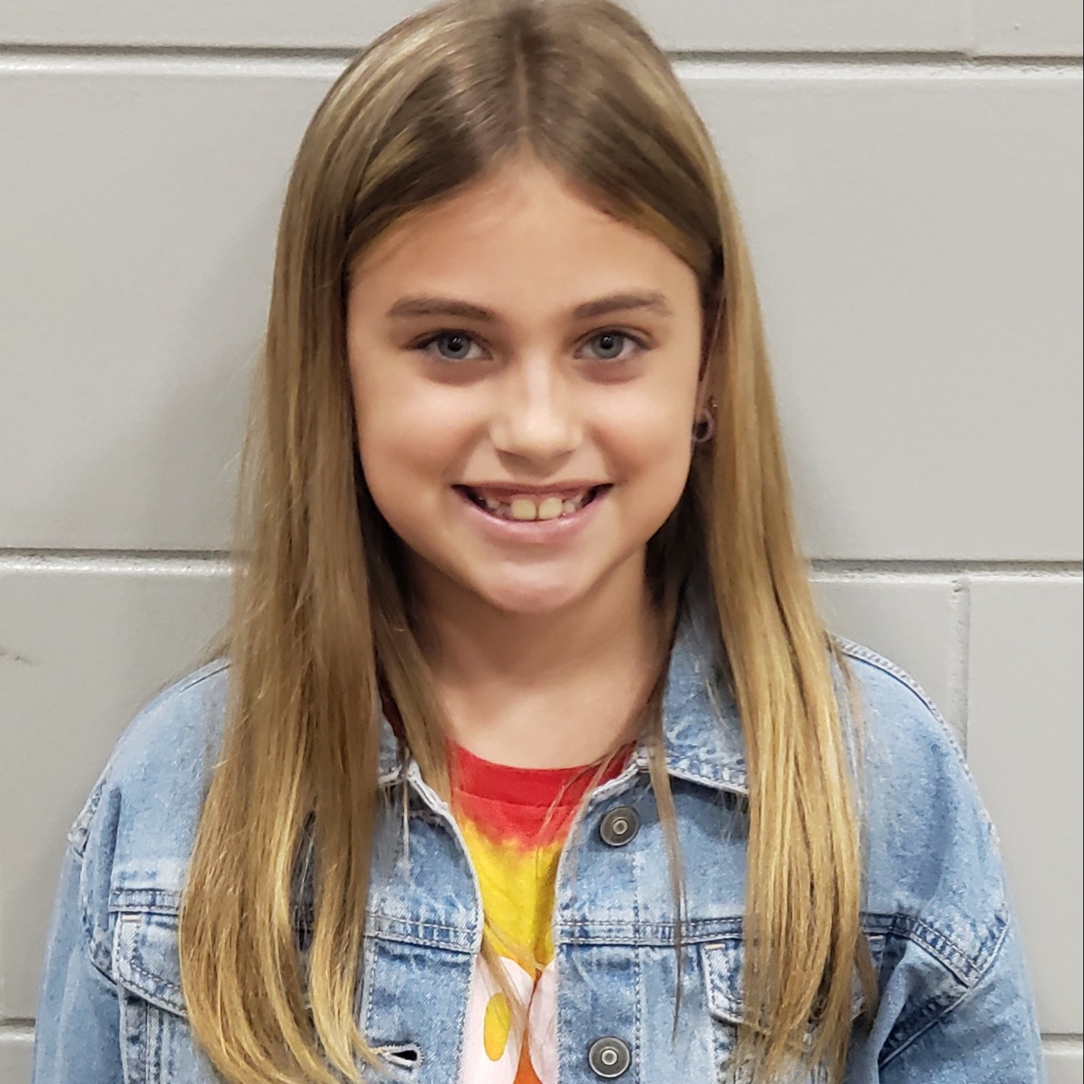 smiling girl with long highlighted blonde hair wearing a red & yellow tie-dyed t-shirt under a faded jean jacket