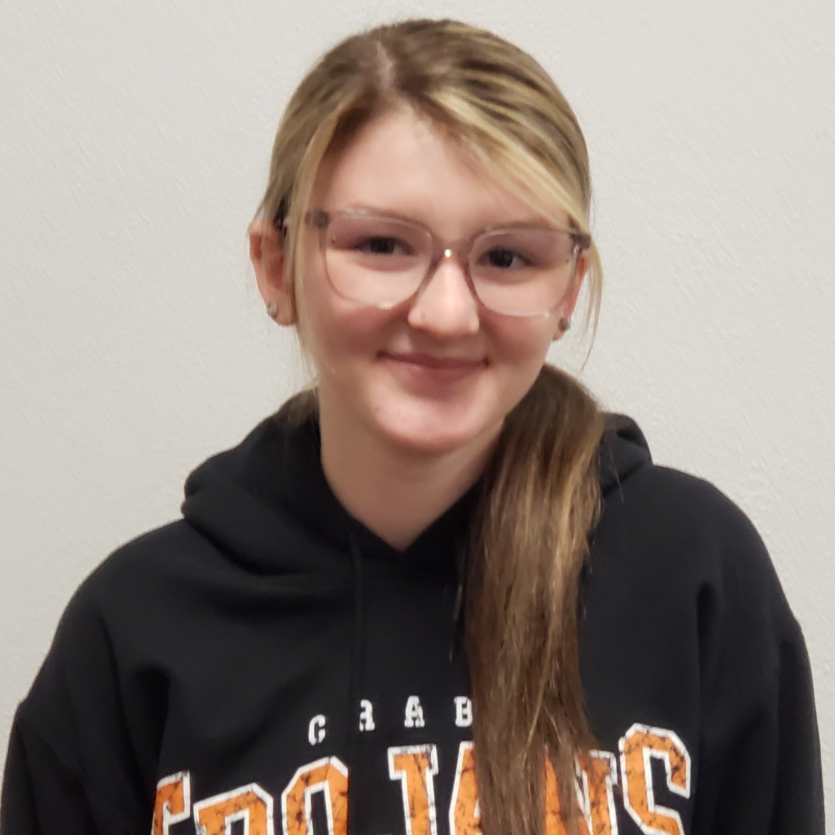 smiling young lady with highlighted blonde hair wearing a black hoodie and glasses