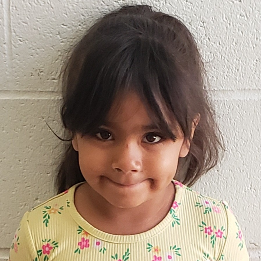 grinning young girl with dark hair pulled back wearing a yellow t-shirt with pink flowers on it