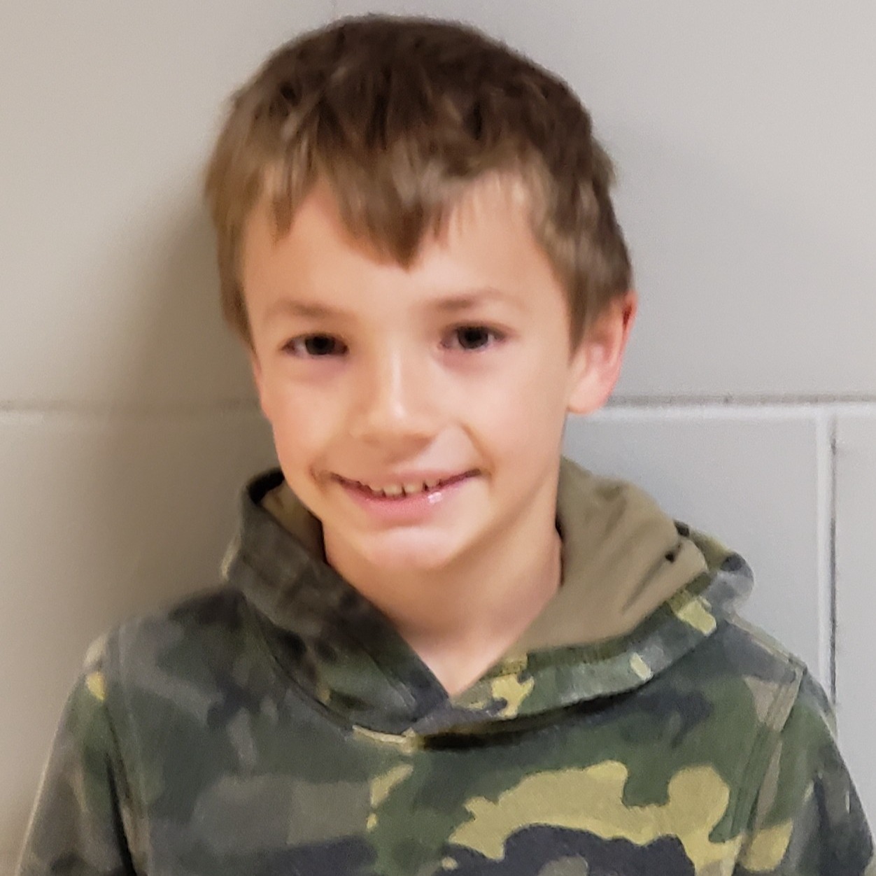 smiling boy with dark blonde hair wearing a camo hoodie