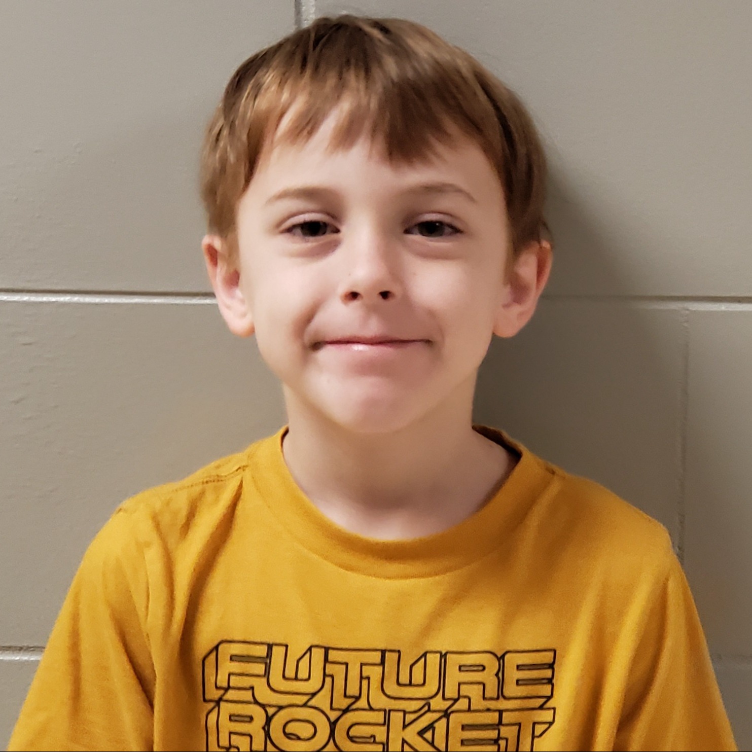 grinning boy with reddish blonde hair wearing a dark yellow t-shirt