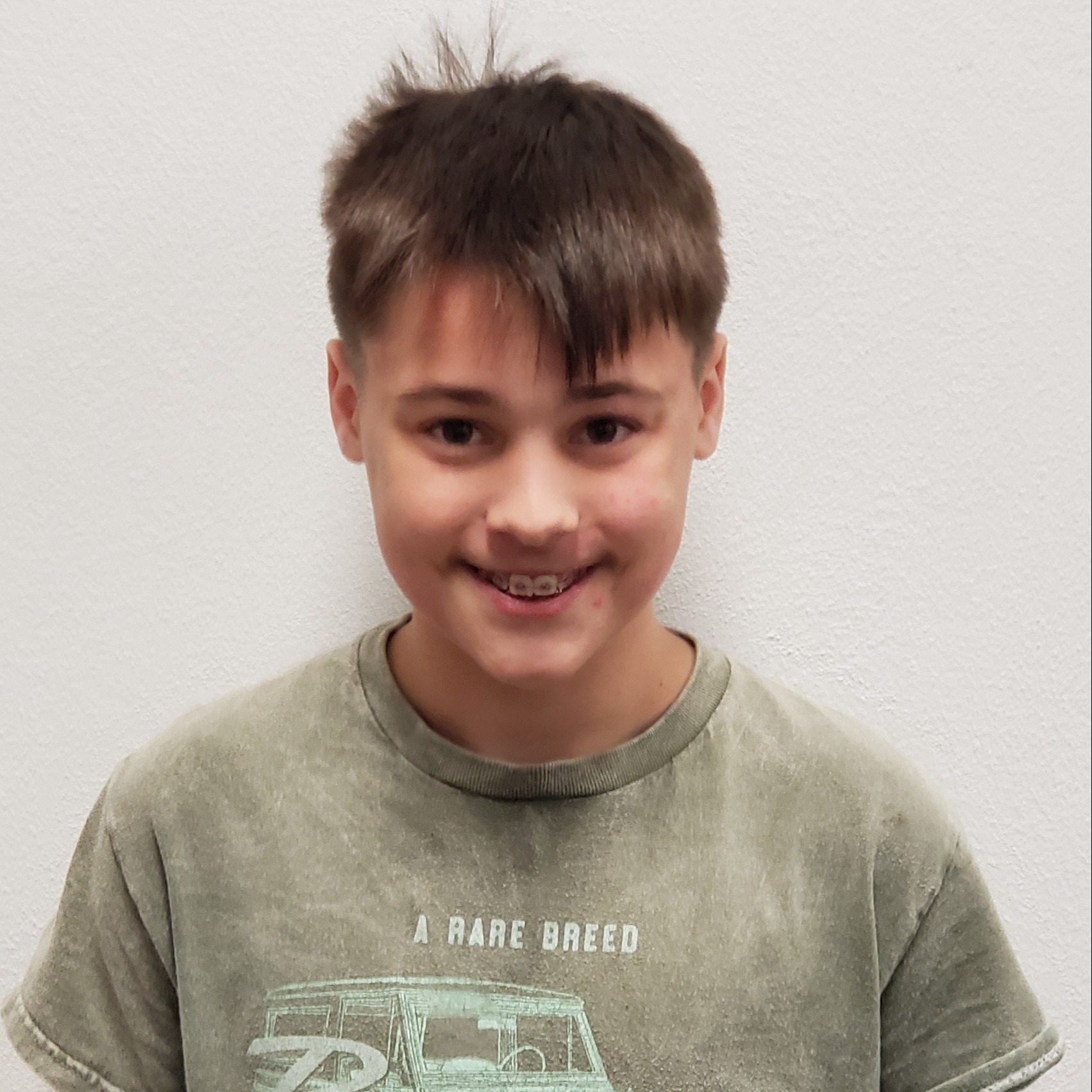 smiling boy with dark spiky hair and braces wearing an olive green t-shirt