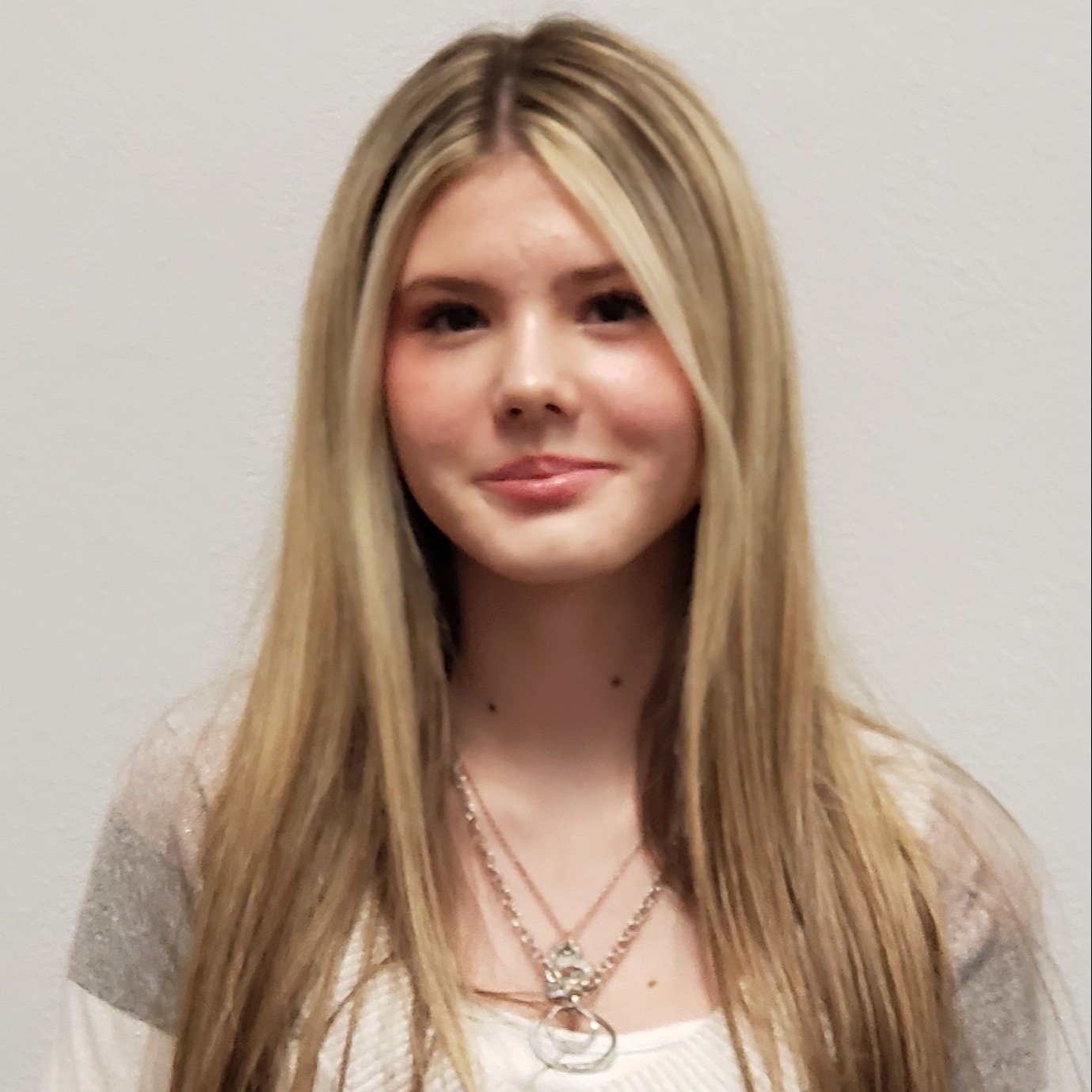 smiling young lady with highlighted blonde hair wearing a tan & white sweater and gold necklaces