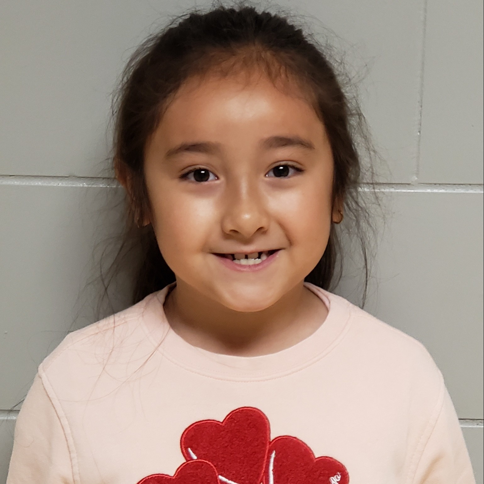 smiling girl with dark hair pulled back wearing a pink t-shirt with hearts on it