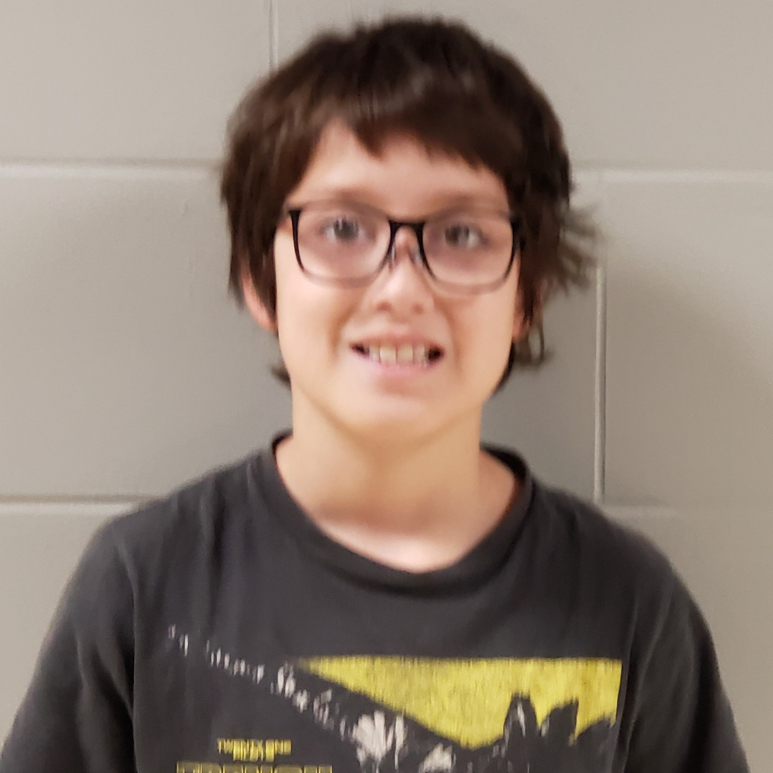smiling boy with dark hair and glasses wearing a gray t-shirt