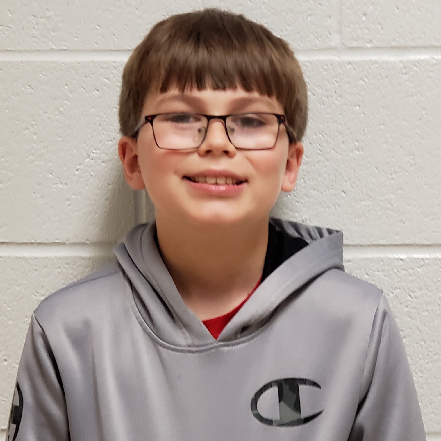 smiling boy with brown hair and glasses wearing a gray hoodie