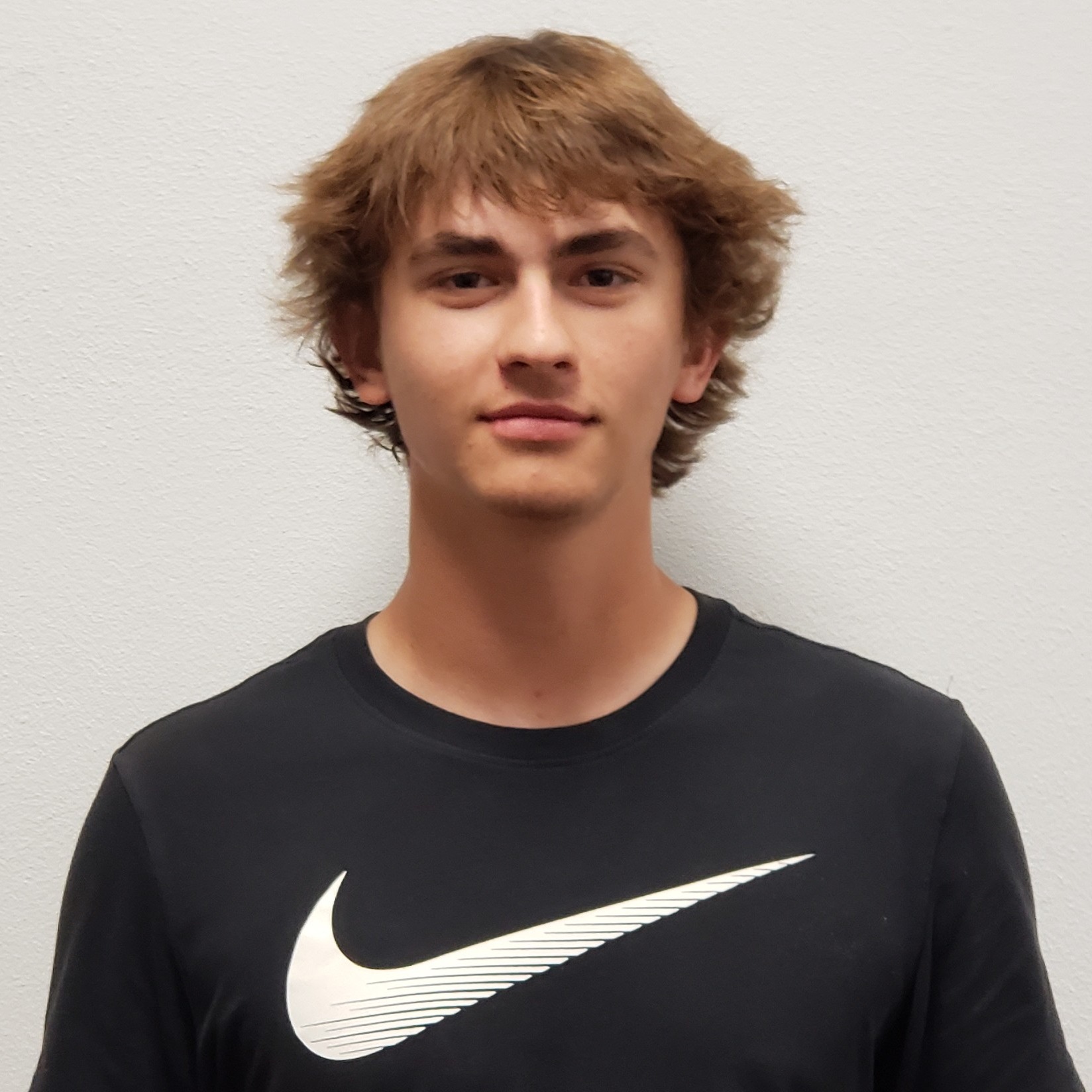 smiling young man with light brown hair wearing a black Nike swoosh t-shirt