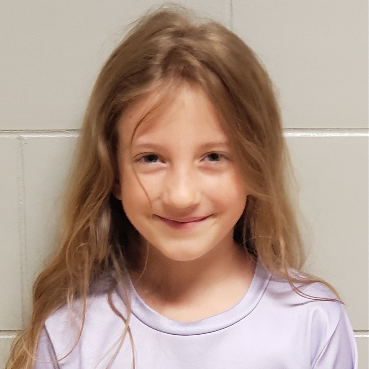 grinning young girl with light brown hair wearing a lilac t-shirt