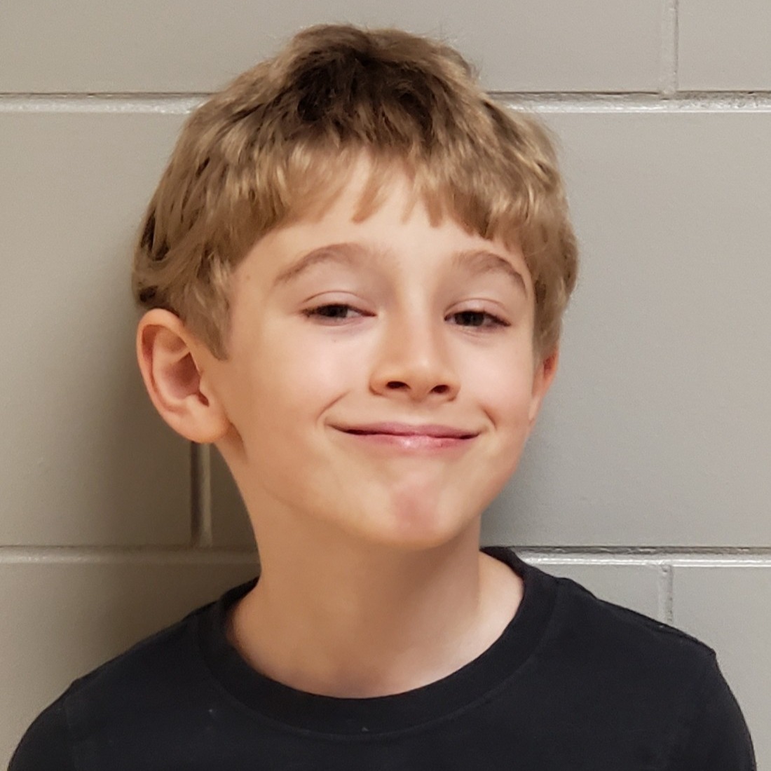 grinning boy with dark blonde hair  wearing a black t-shirt 