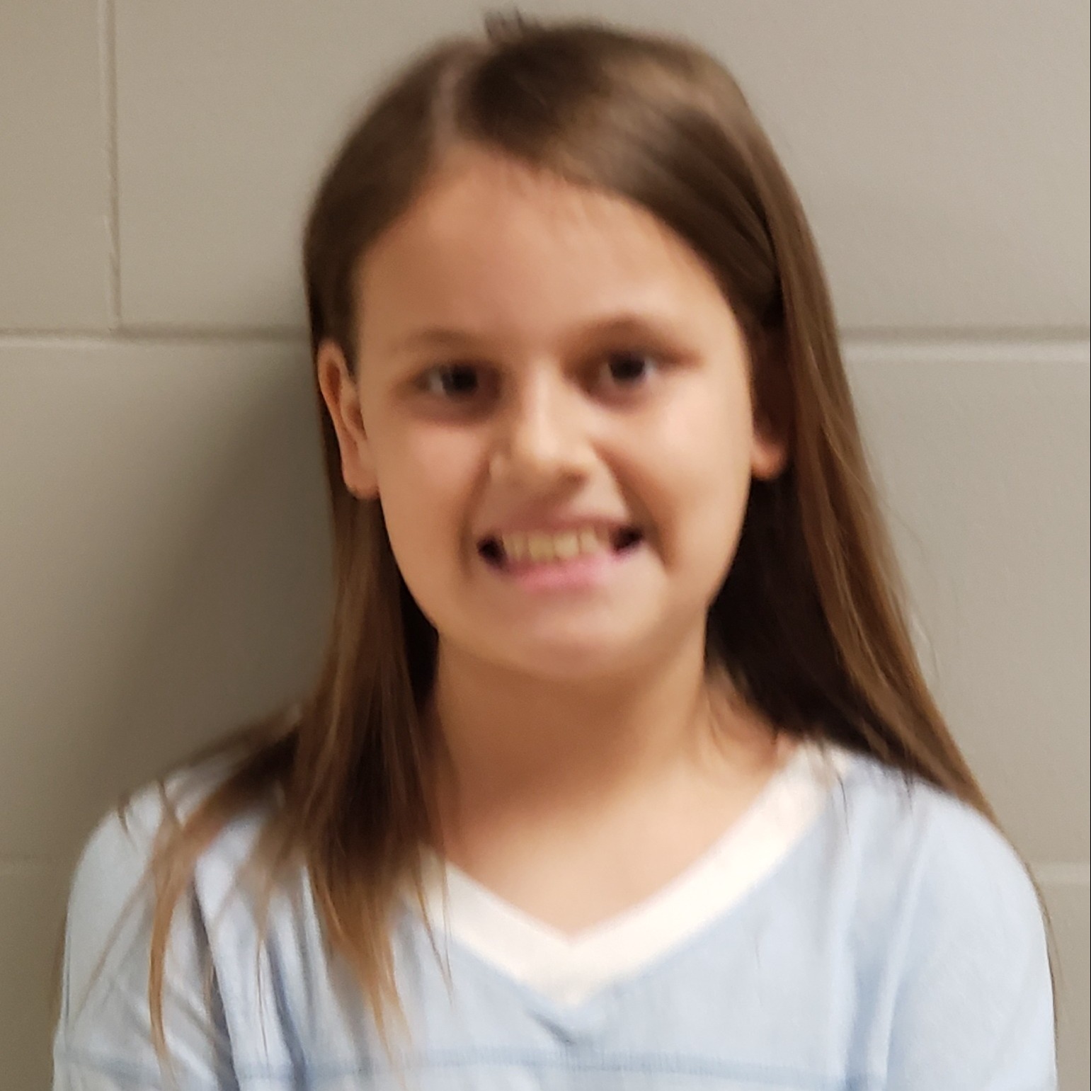 smiling  girl with brown hair wearing a light blue t-shirt