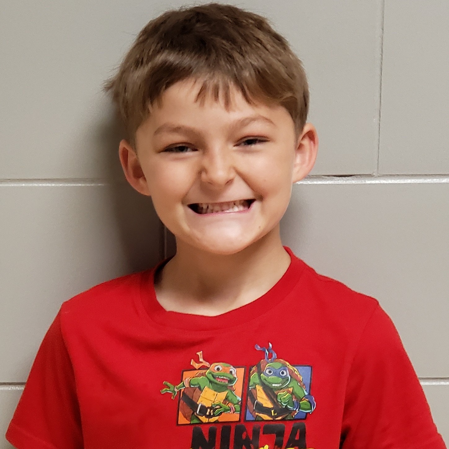 smiling young boy with light brown hair wearing a red t-shirt