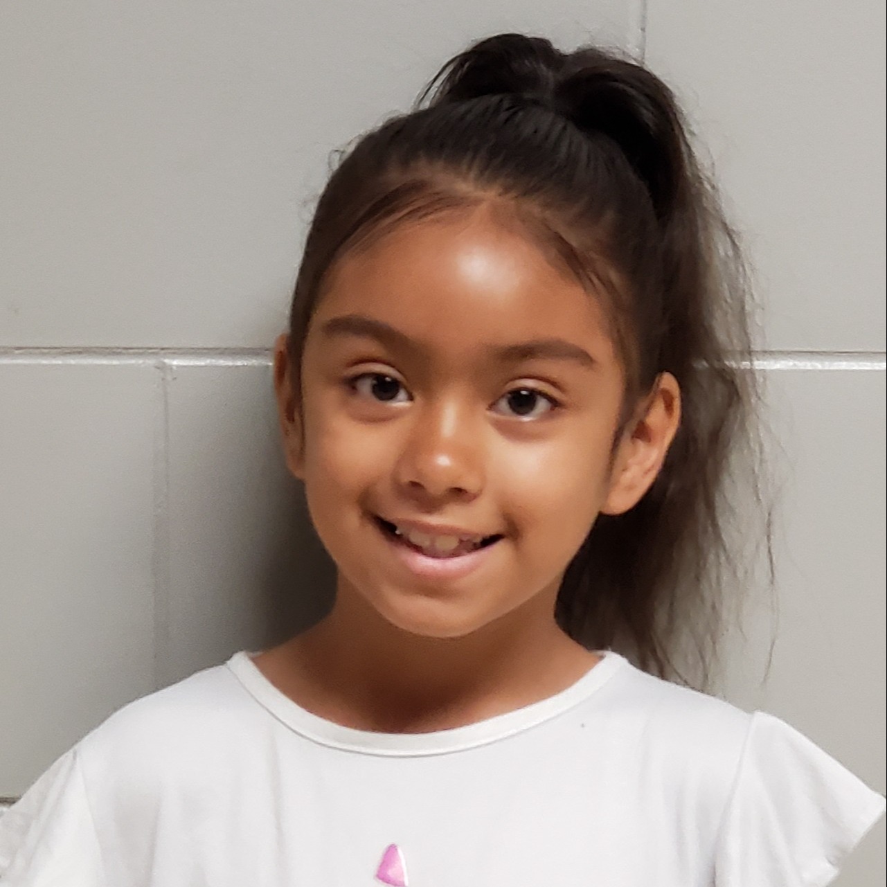 smiling young girl with dark hair pulled back wearing a white t-shirt