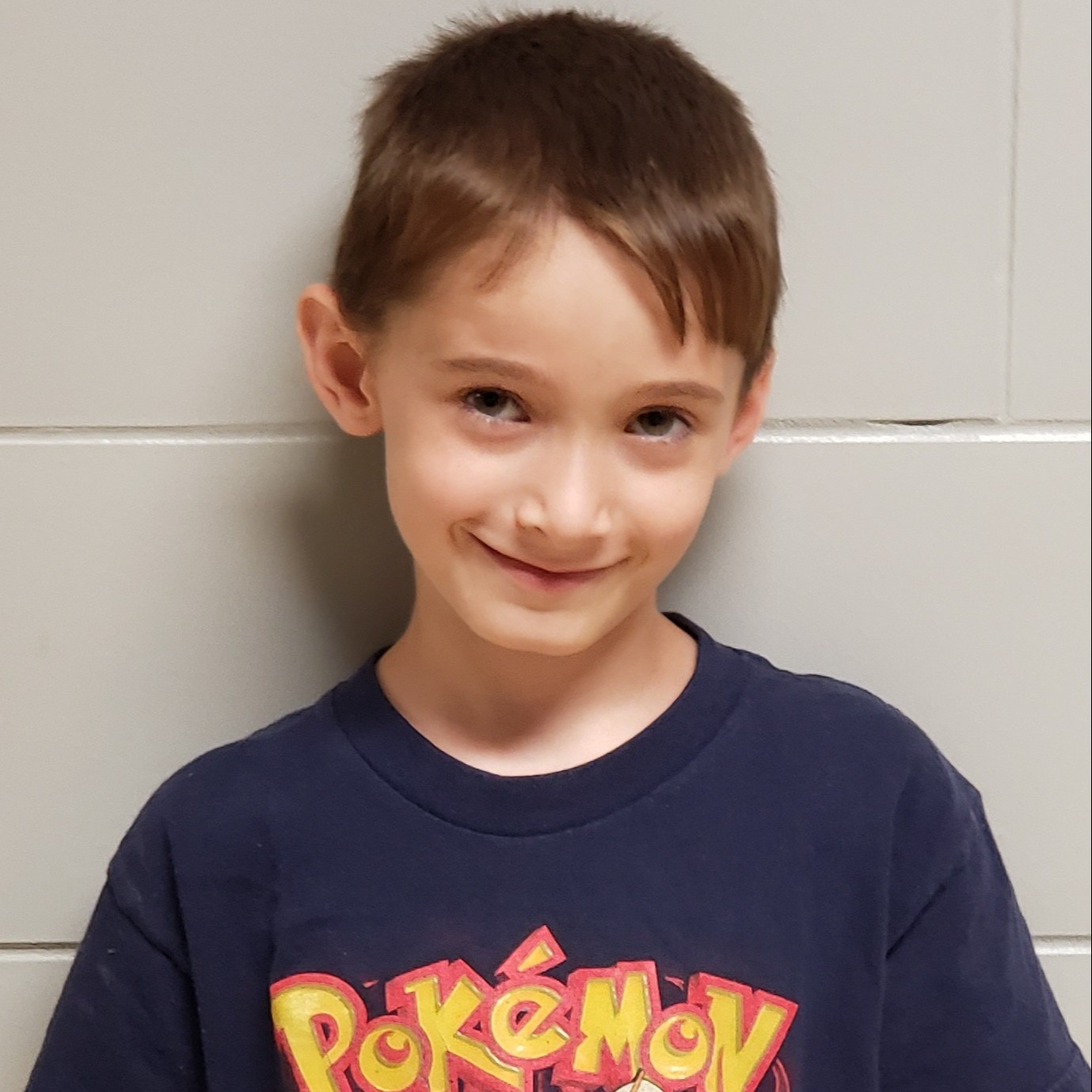 grinning young boy with brown hair wearing a navy Pokemon t-shirt