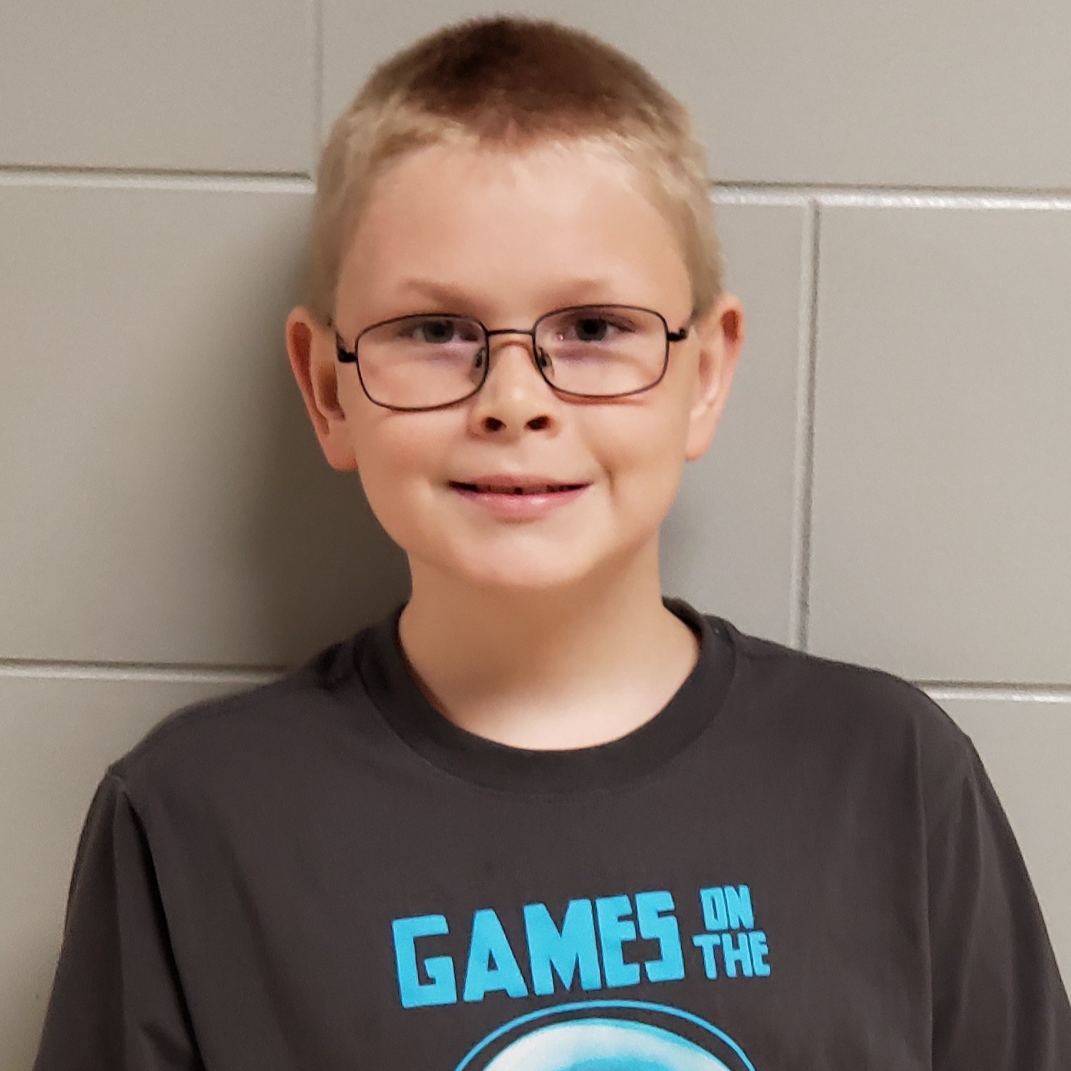 boy with blonde hair and glasses wearing a dark gray t-shirt