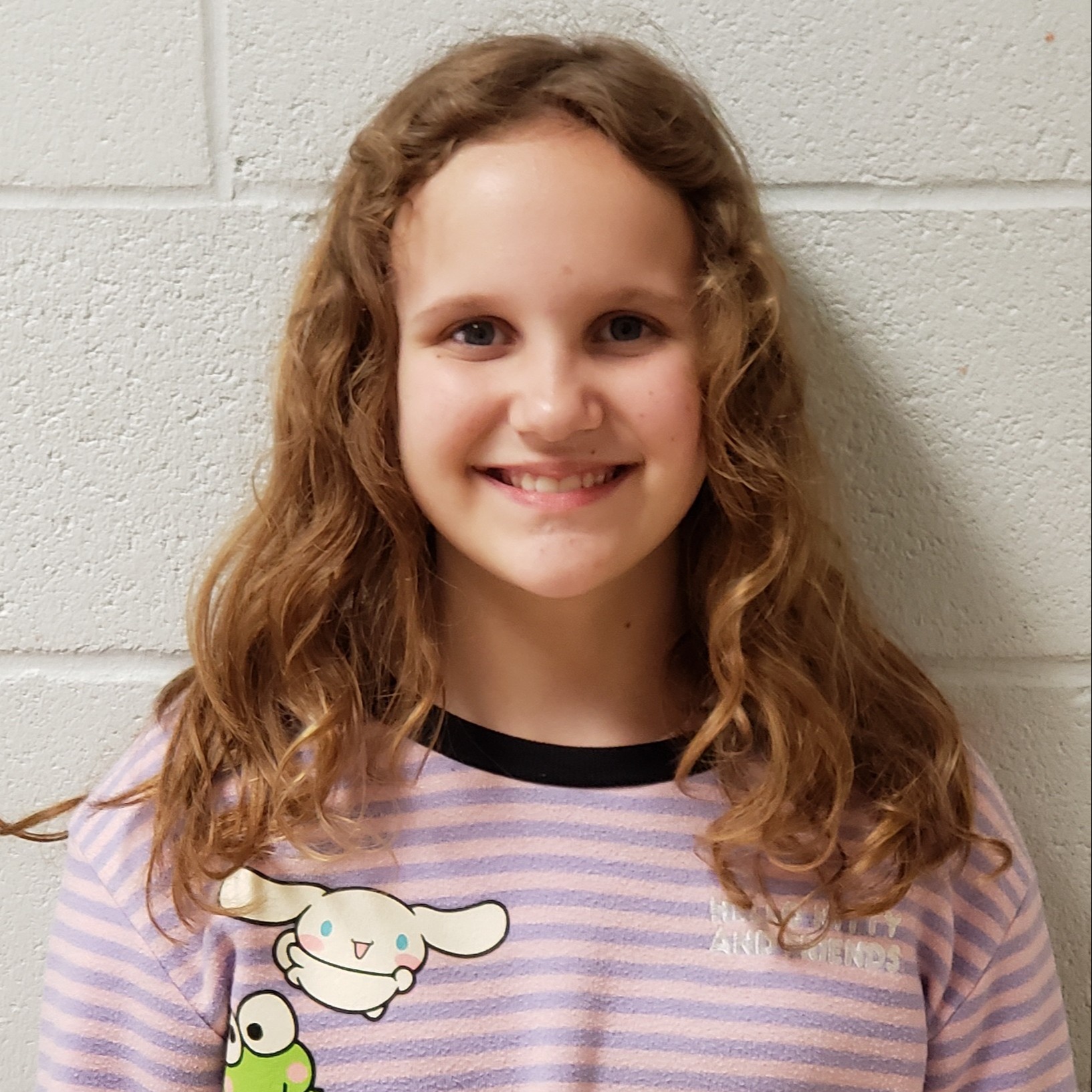 smiling girl with long, curly dark blonde hair wearing a pink & purple stripled sweatshirt