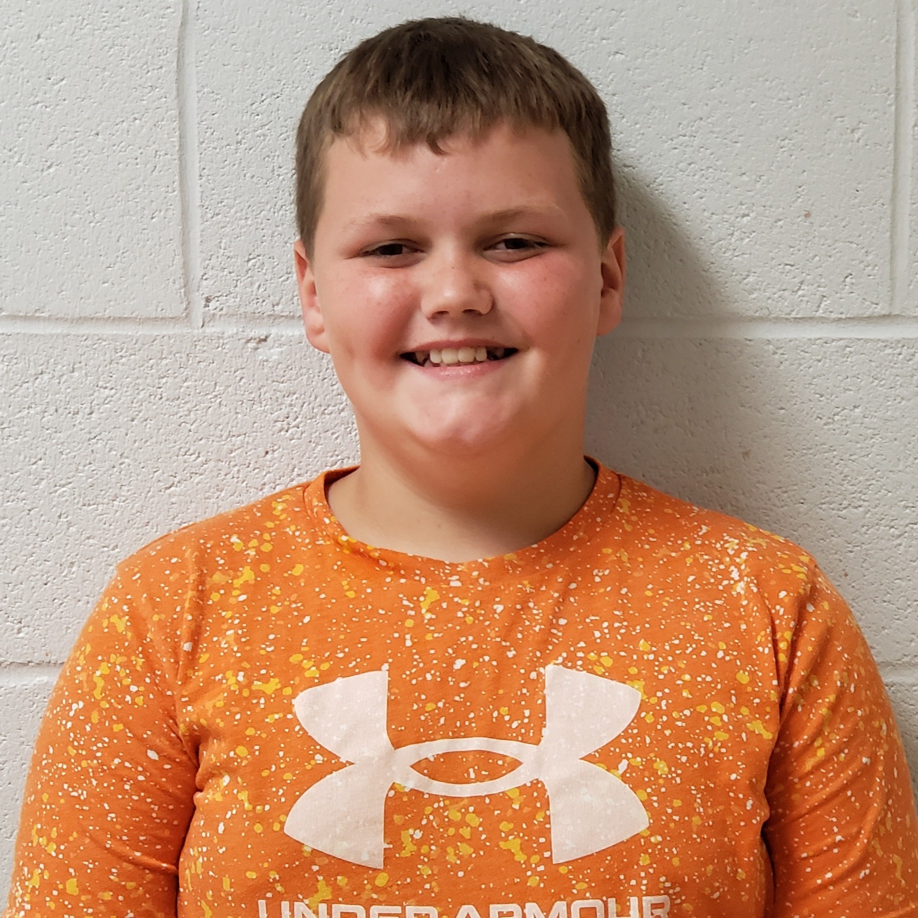 smiling boy with brown hair wearing an orange speckled UnderArmor t-shirt