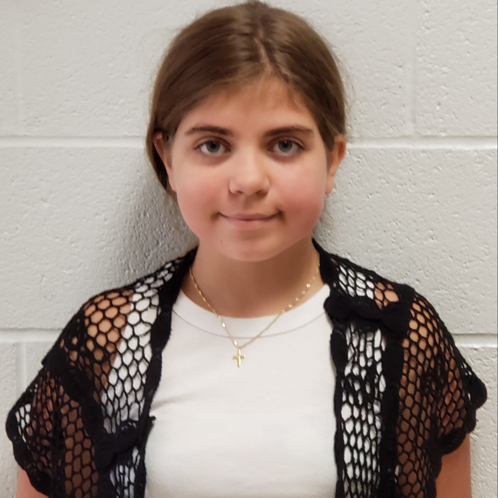 girl with brown hair pulled back wearing a white tank top under a black mesh cardigan