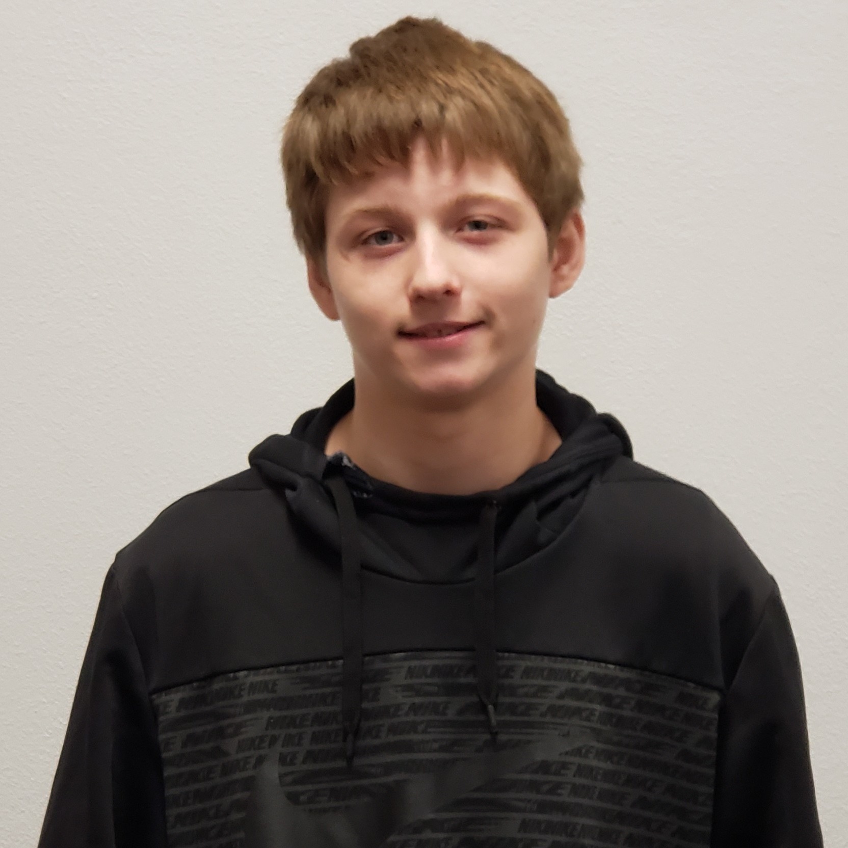 grinning boy with dark blonde hair wearing a dark gray hoodie