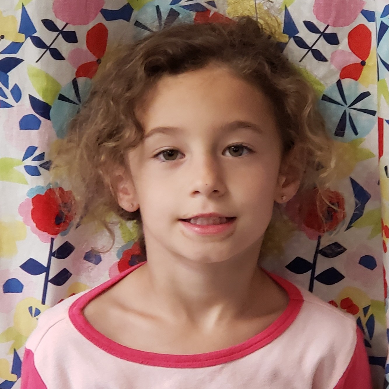 young girl with wavy hair pulled back wearing pink pajamas