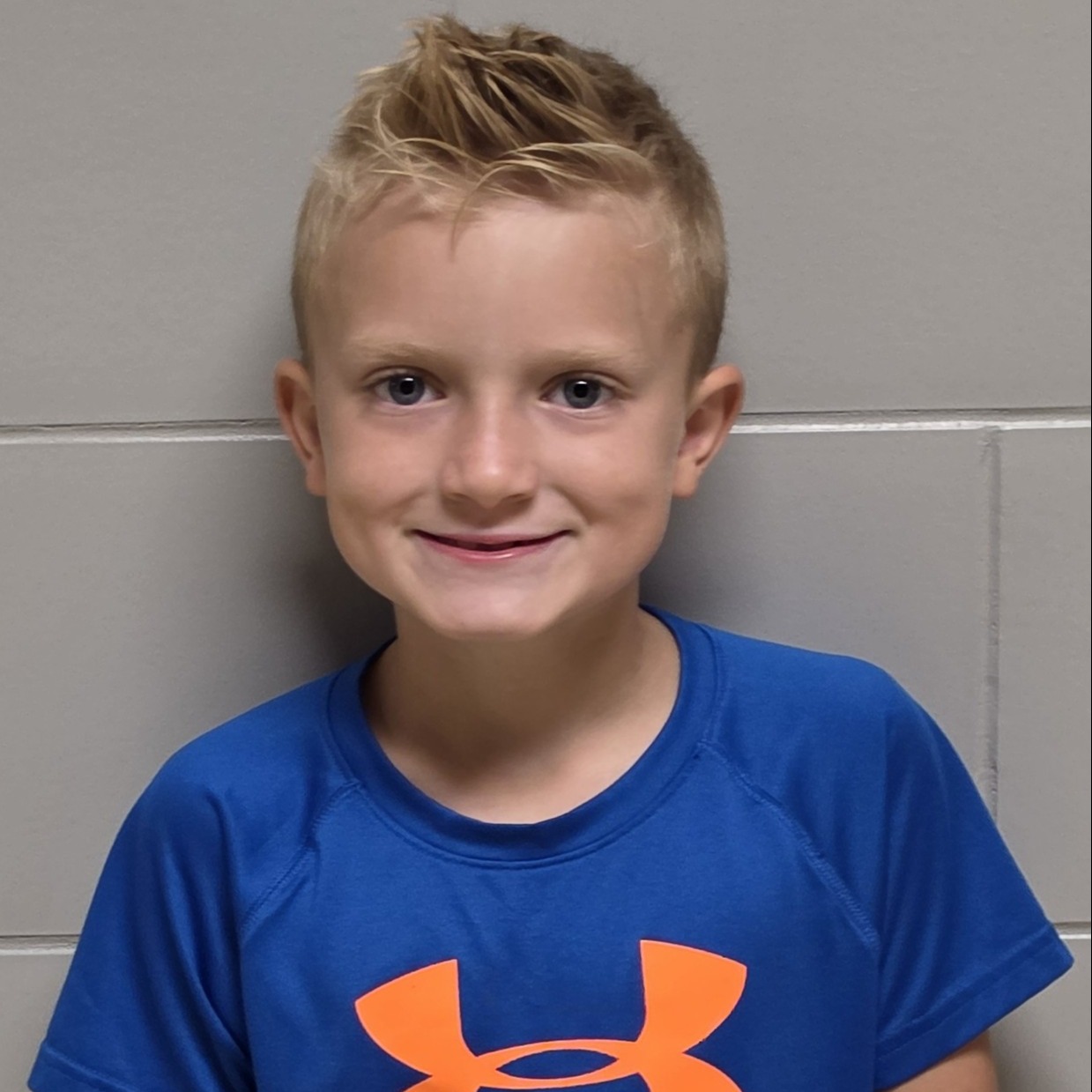 smiling young boy with spiky blonde hair wearing a blue t-shirt