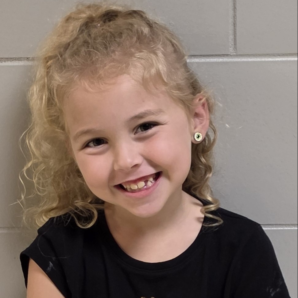 smiling young girl with curly blonde hair wearing a black t-shirt