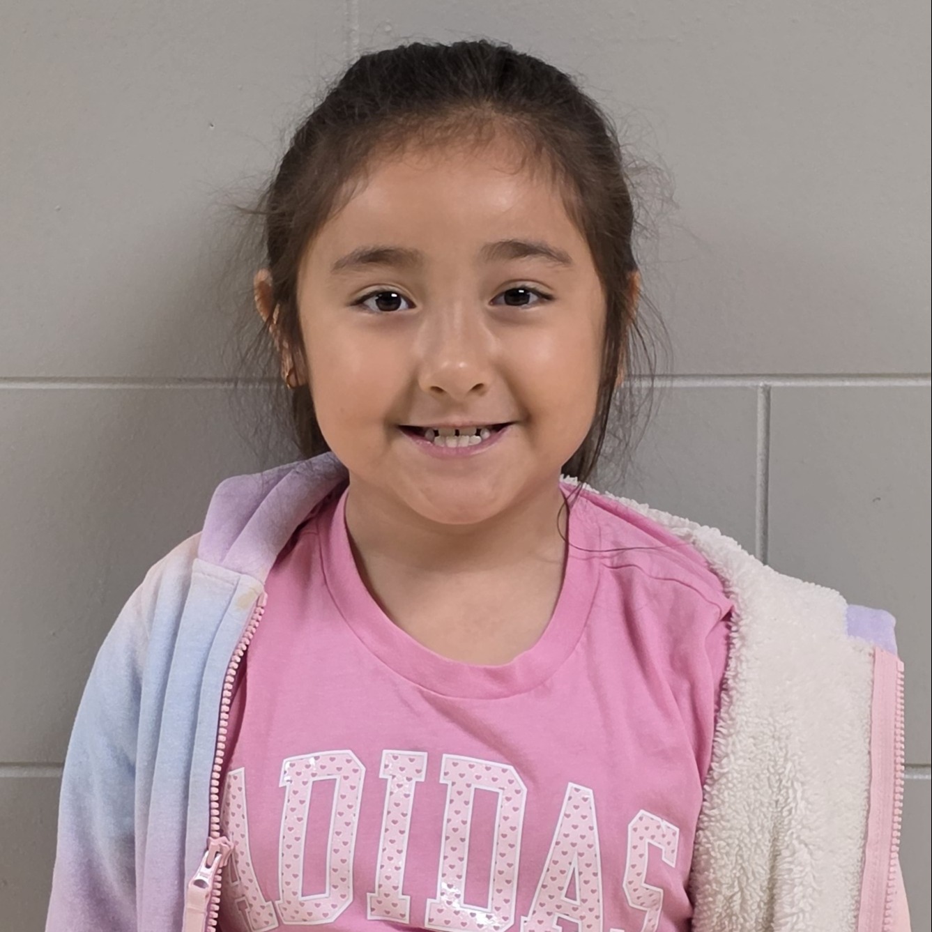 smiling girl with brown hair pulled back wearing a pink t-shirt under a light pink & lilac jacket