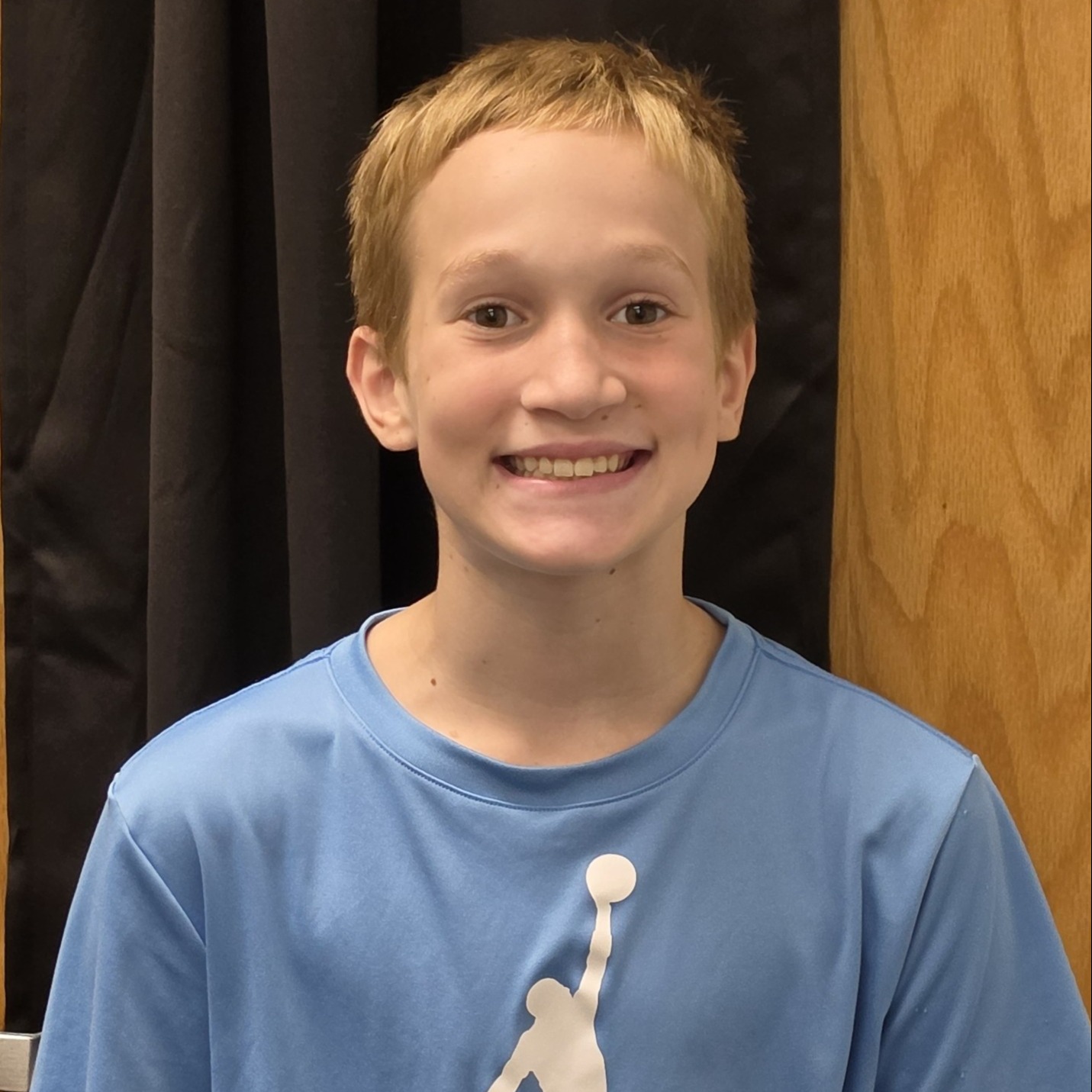 smiling boy with blonde hair wearing a light blue Jordan t-shirt