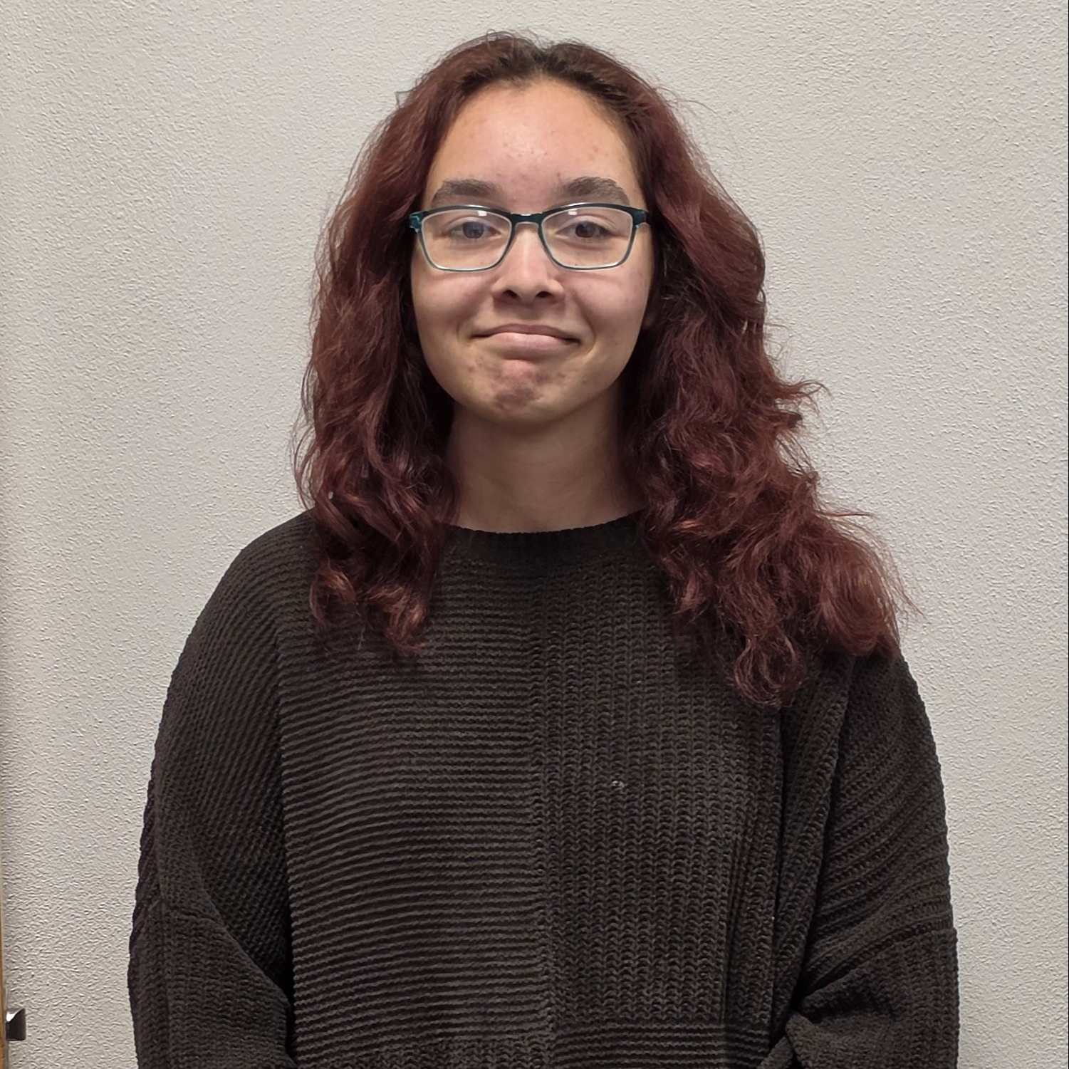 grinning girl with auburn hair and glasses wearing a dark gray sweater