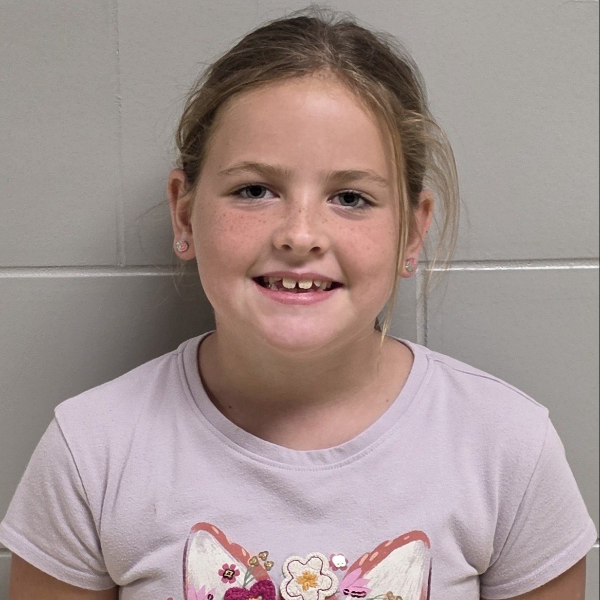 smiling girl with sandy hair pulled back and freckles wearing a lilac t-shirt