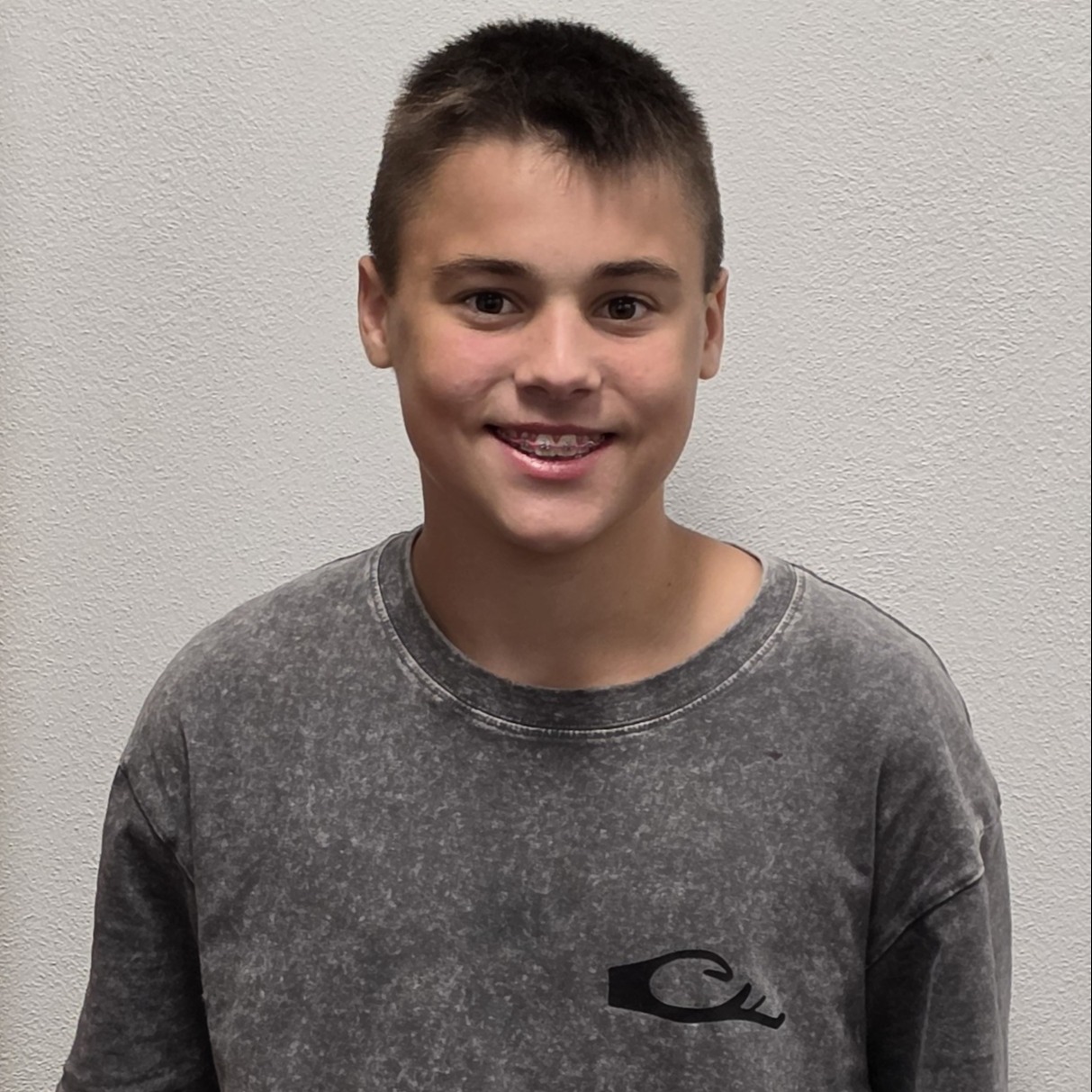 smiling boy with spiky black hair and braces wearing a dark gray t-shirt