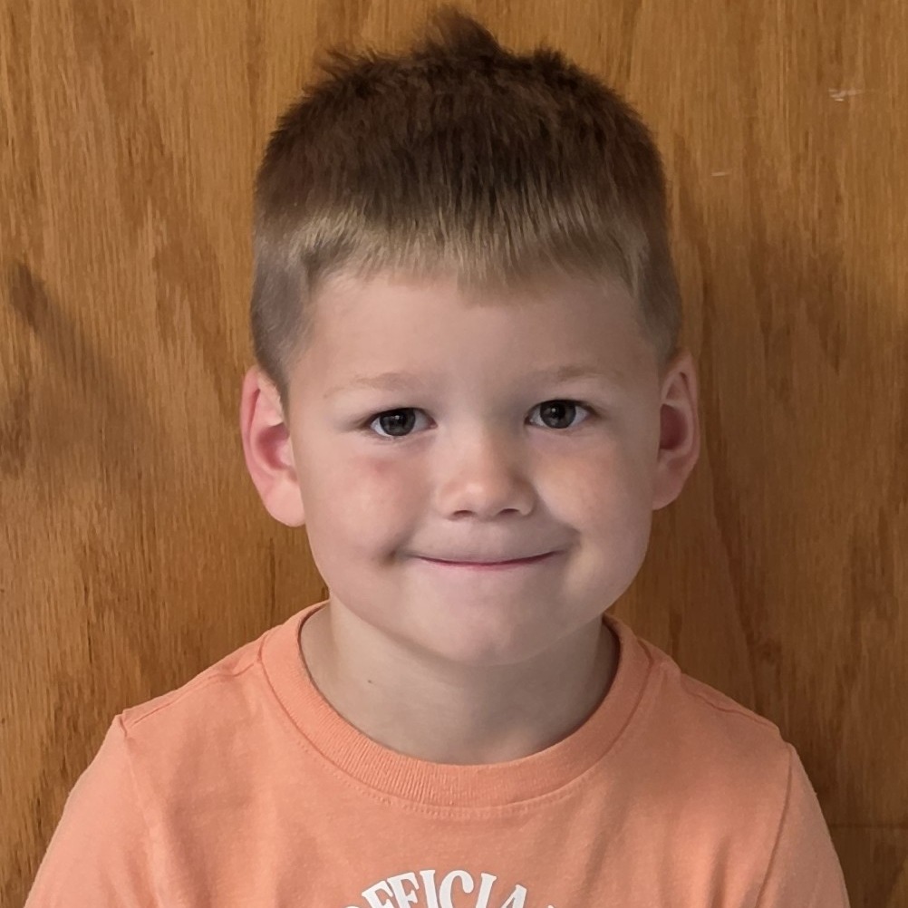 grinning young boy with sandy blonde hair wearing a light orange t-shirt