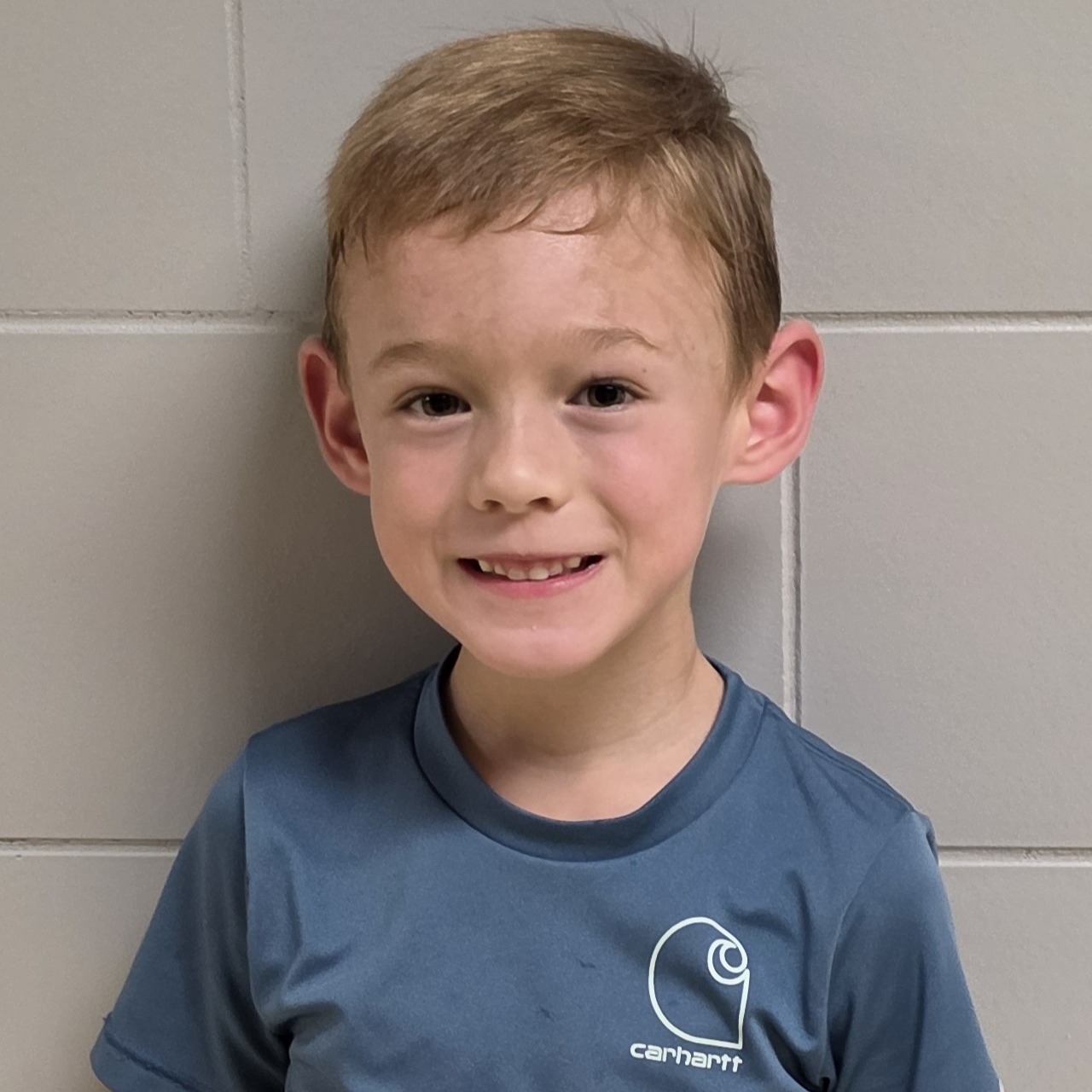 smiling boy with blonde hair wearing  a blue t-shirt