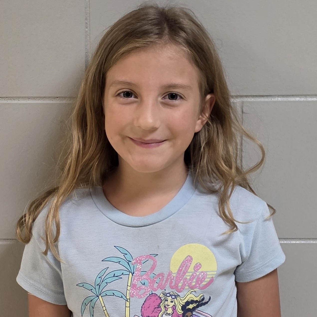 smiling girl with sandy hair wearing a light blue Barbie t-shirt